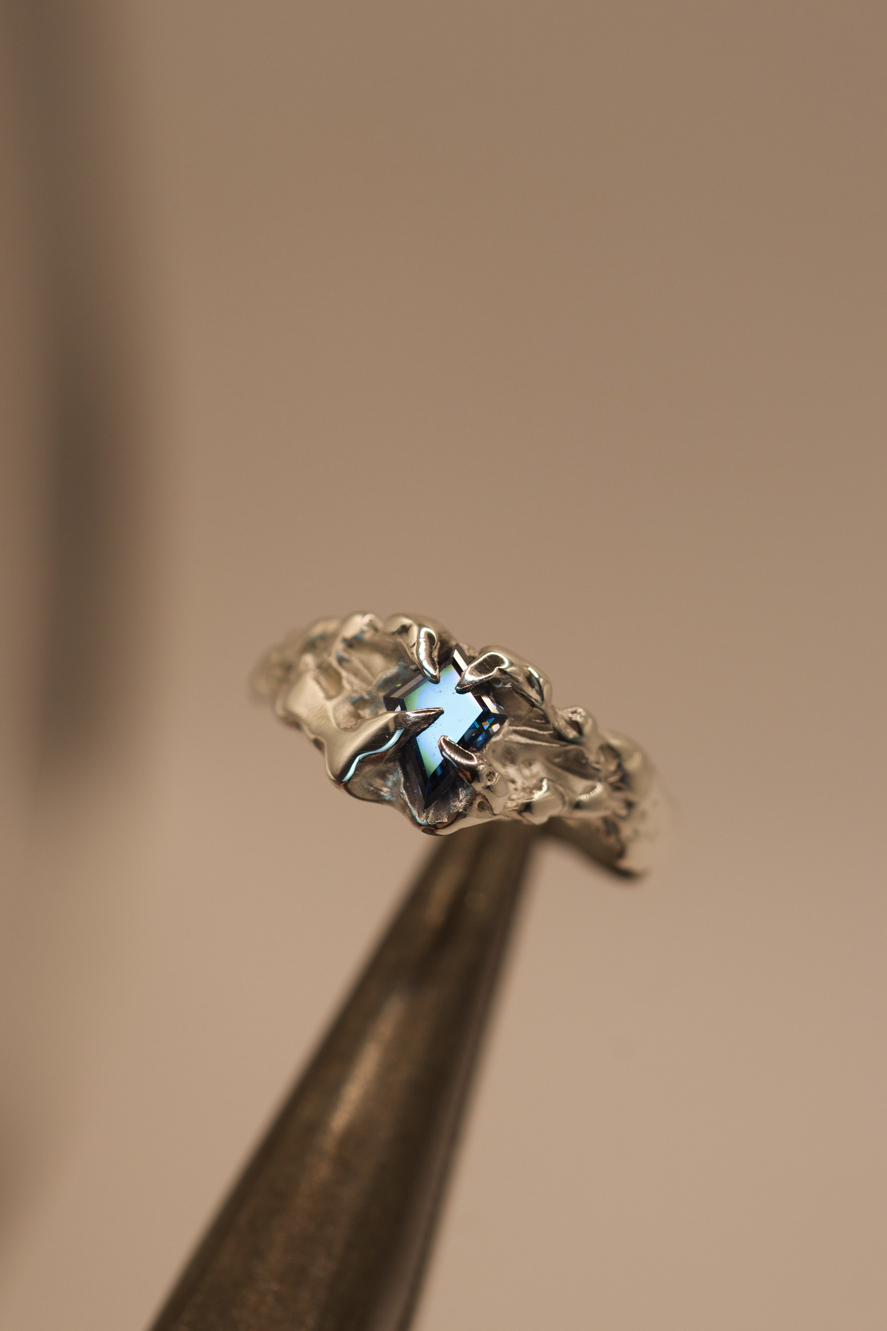 Crafted with the lost wax technique, this handmade sterling silver ring features a bold vivid blue kite cut moissanite set in gothic inspired claws, with molten, organic textures for an alternative style.