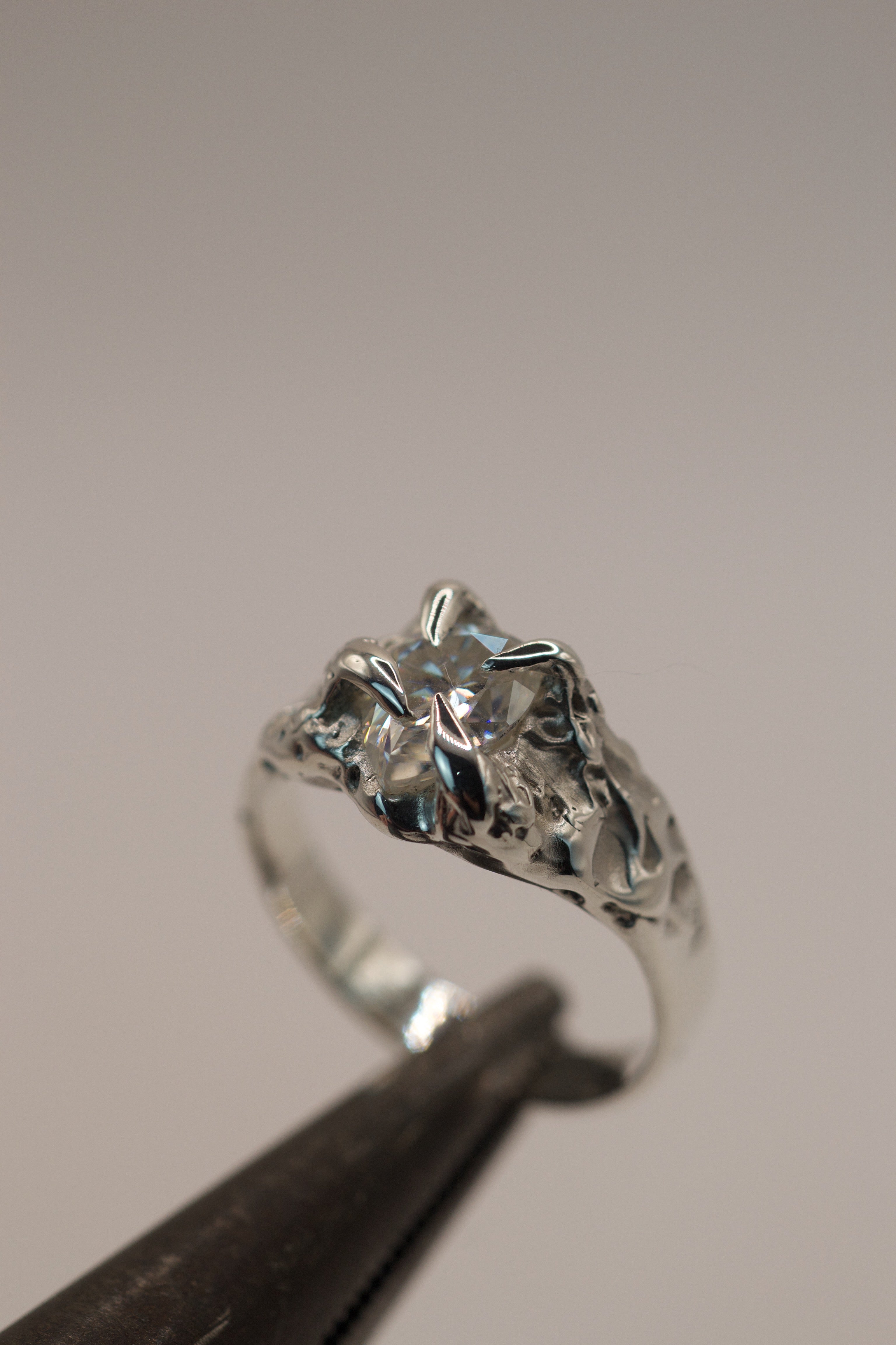 Handmade sterling silver organic alternative engagement ring with gothic inspired claws holding a pear cut moissanite, crafted using the lost wax method.