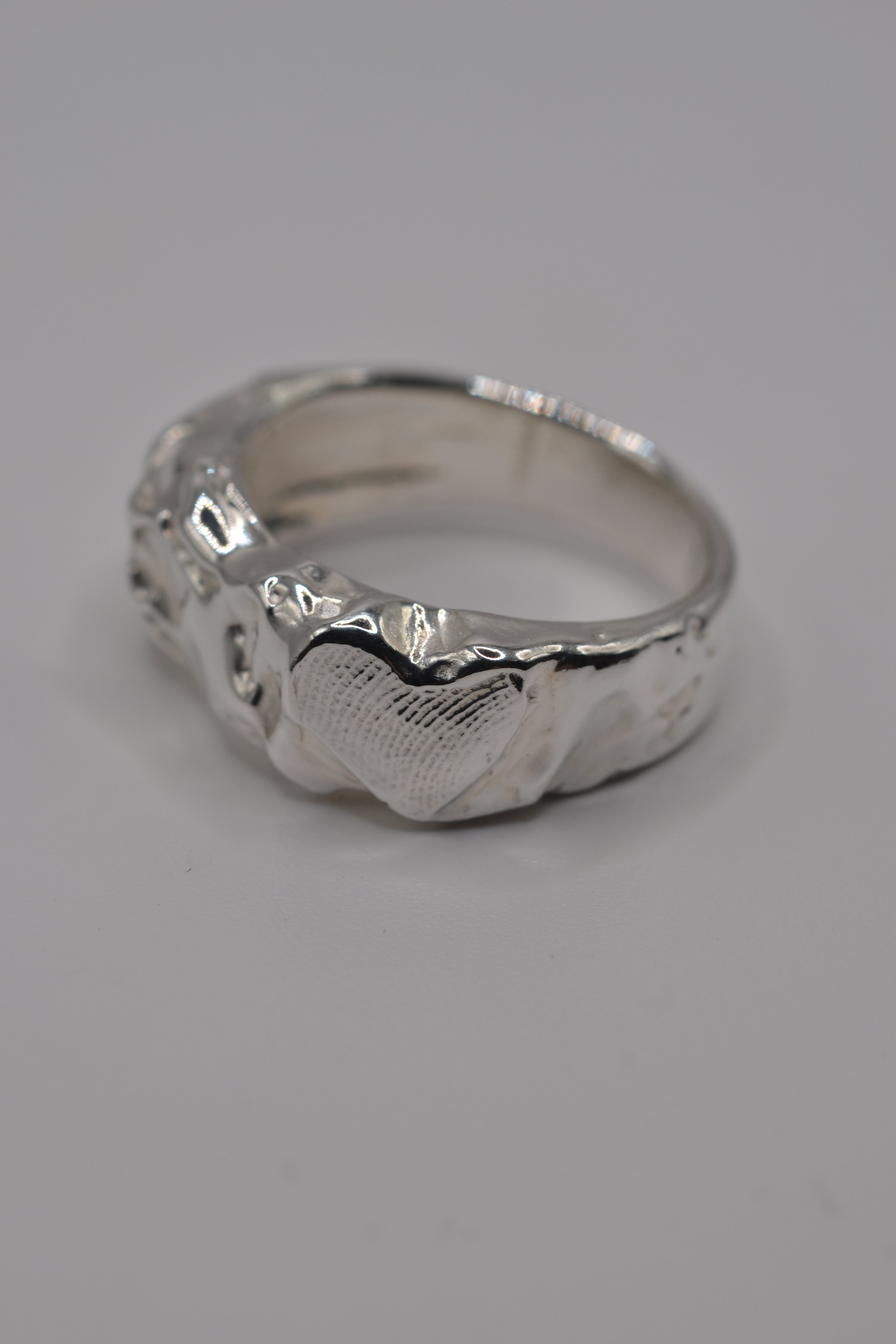 A textured sterling silver ring with a hammered and polished organic surface, shown on a neutral light gray background.
