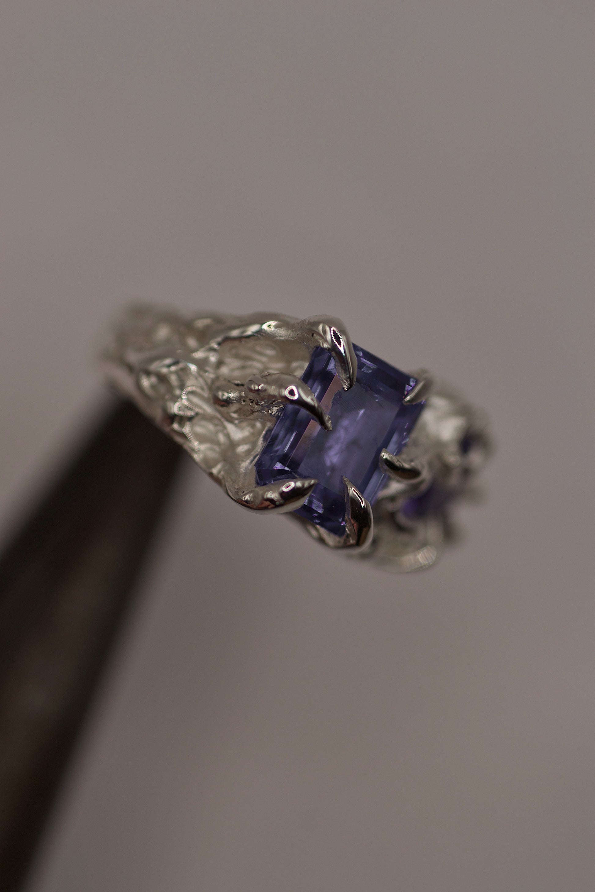 Side view of the ring on a hand, displaying the sharp, claw-like prongs and deeply set purple stones. The organic texture of the silver surface is consistent with lost wax casting craftsmanship.