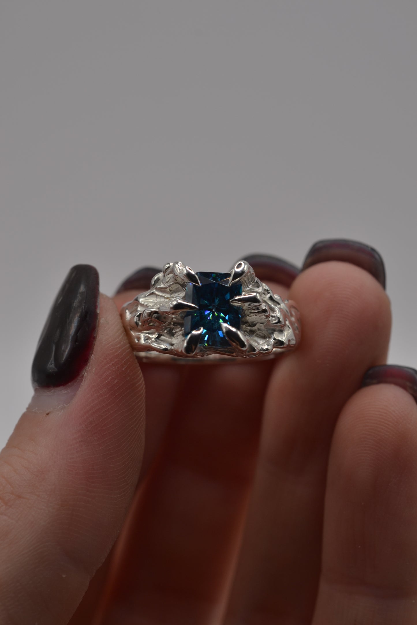 Close-up of a handmade alternative silver ring featuring a blue radiant cut moissanite, created using the lost wax casting technique.