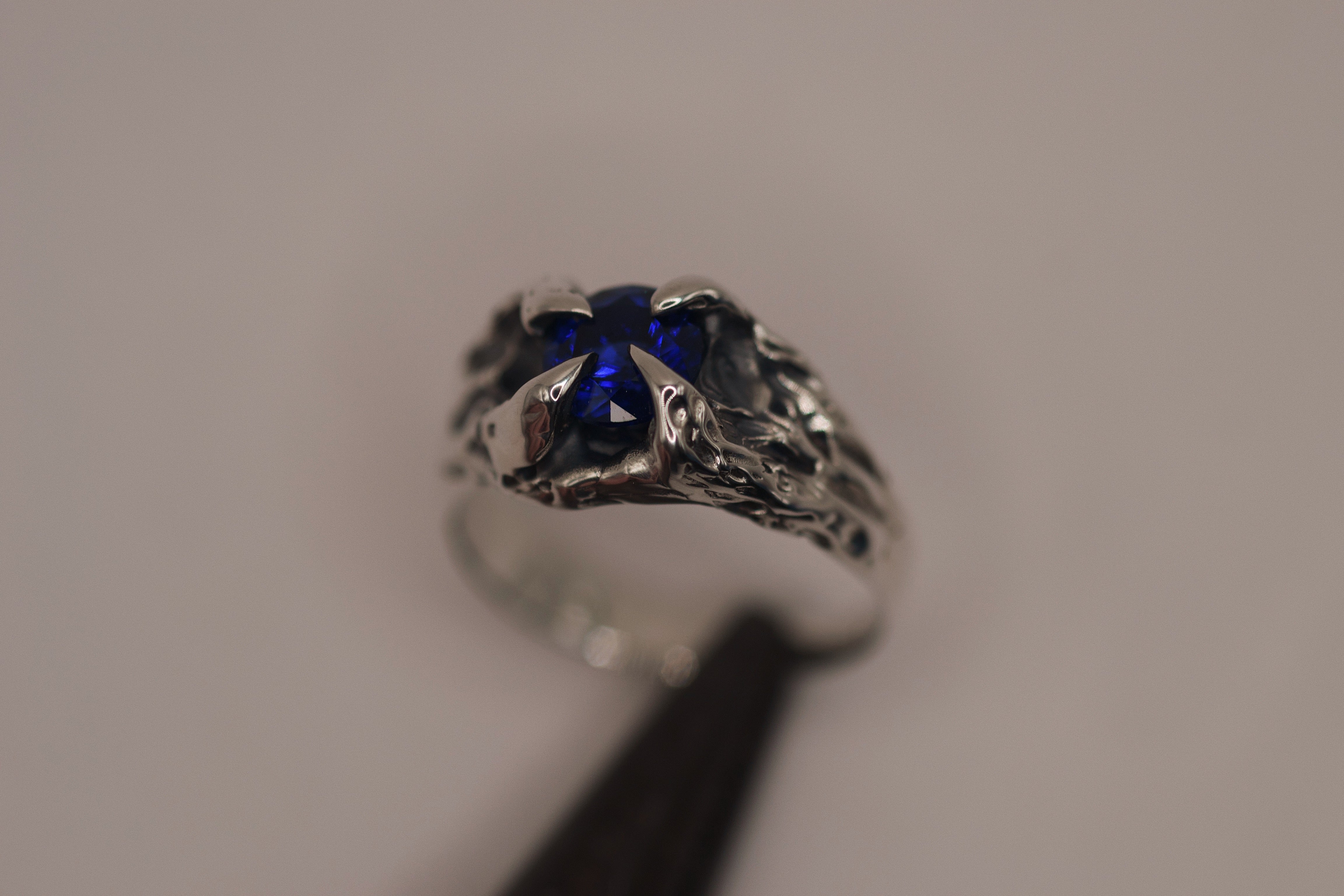 Gothic-style silver ring with strong claw settings holding a round sapphire, sculpted using the lost wax method for a raw, handmade finish.