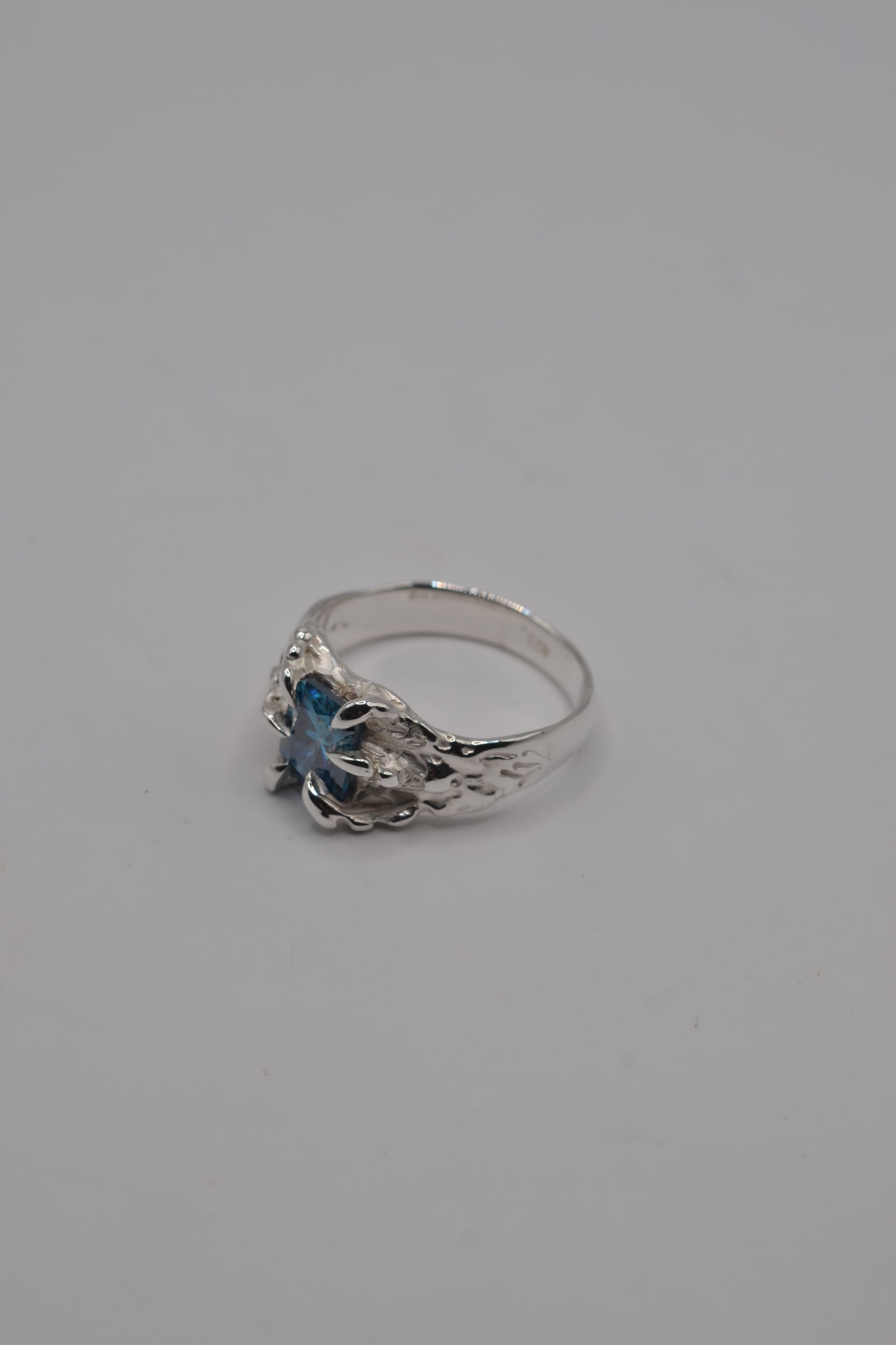 Side profile of a lost wax cast silver ring featuring a blue radiant cut moissanite in an alternative jewellery style.