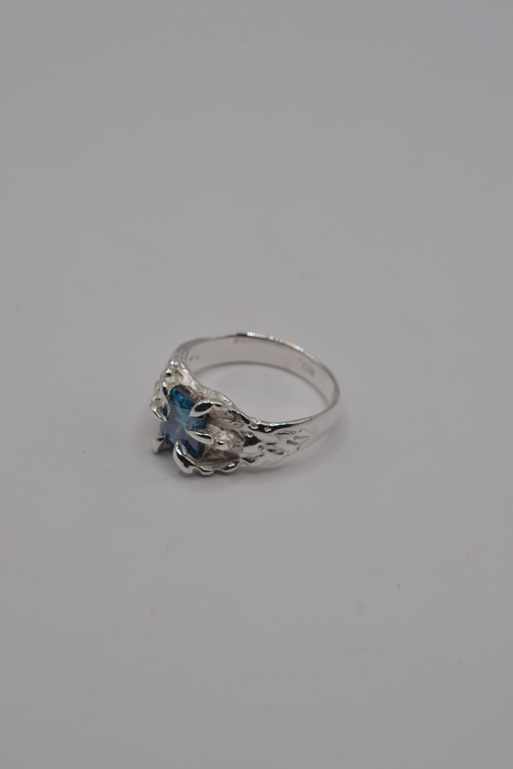 Side profile of a lost wax cast silver ring featuring a blue radiant cut moissanite in an alternative jewellery style.