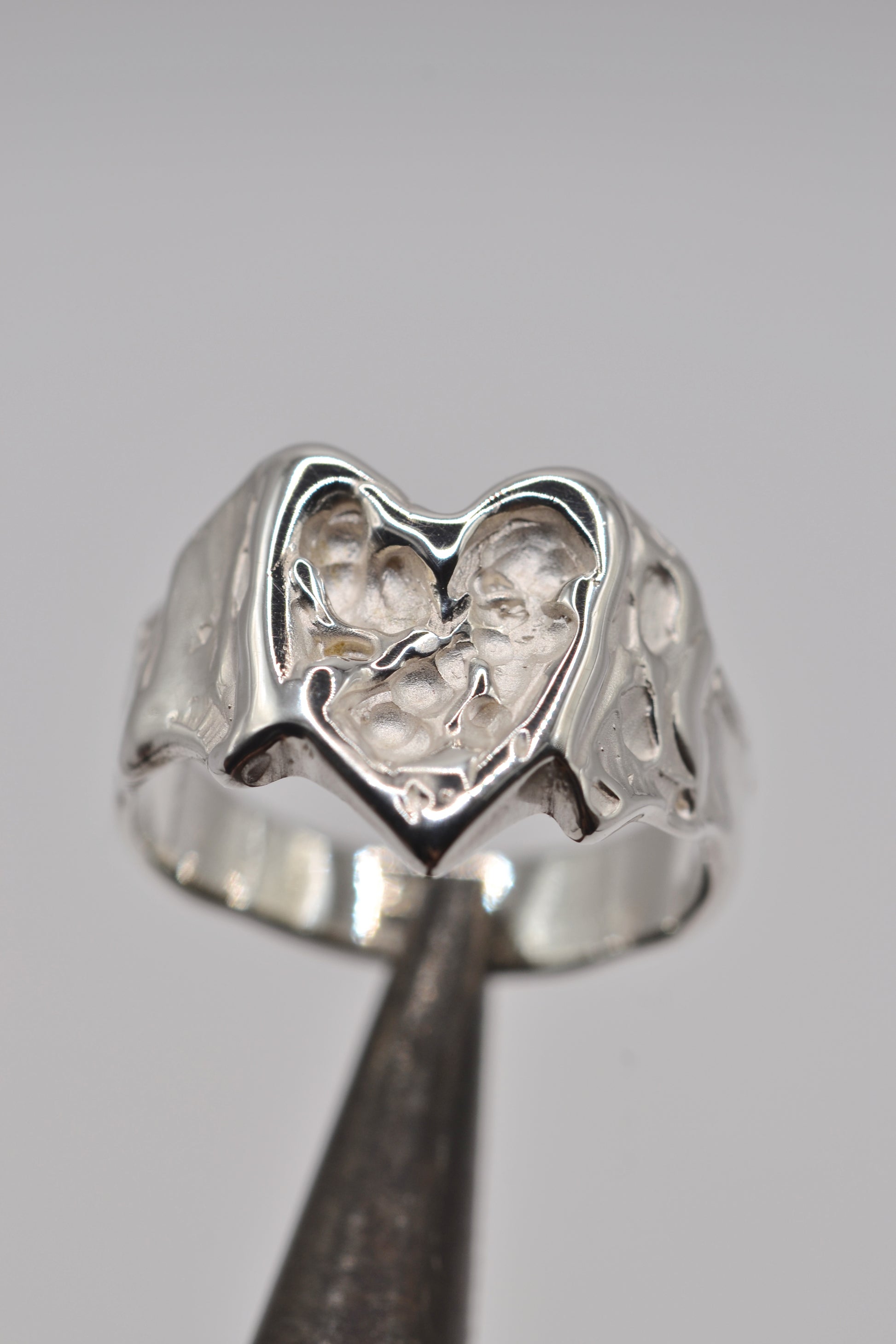 Silver lost wax ring with organic heart design on a gray background