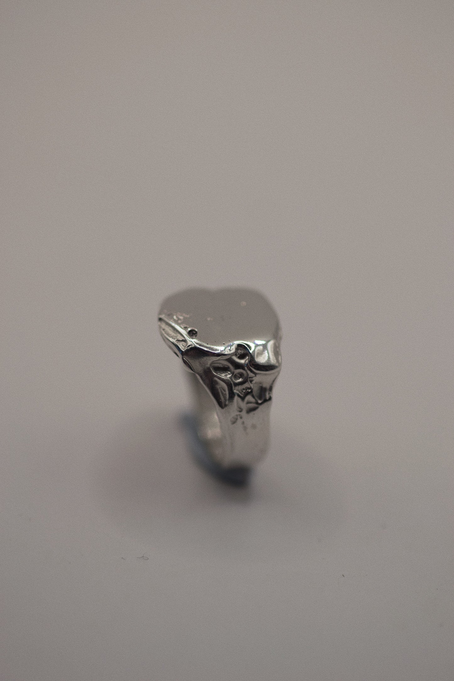 Handmade from solid 925 sterling silver, this signet ring is marked by organic dips and grooves that provide a textured, rugged finish. The smooth band of the ring leads to an intentionally uneven surface, where the dips and craters add character and depth. The silver’s natural imperfections make it a striking piece, offering an earthy look that’s refined yet grunge-inspired. This ring is cast using the lost wax method, making it a one-of-a-kind piece.