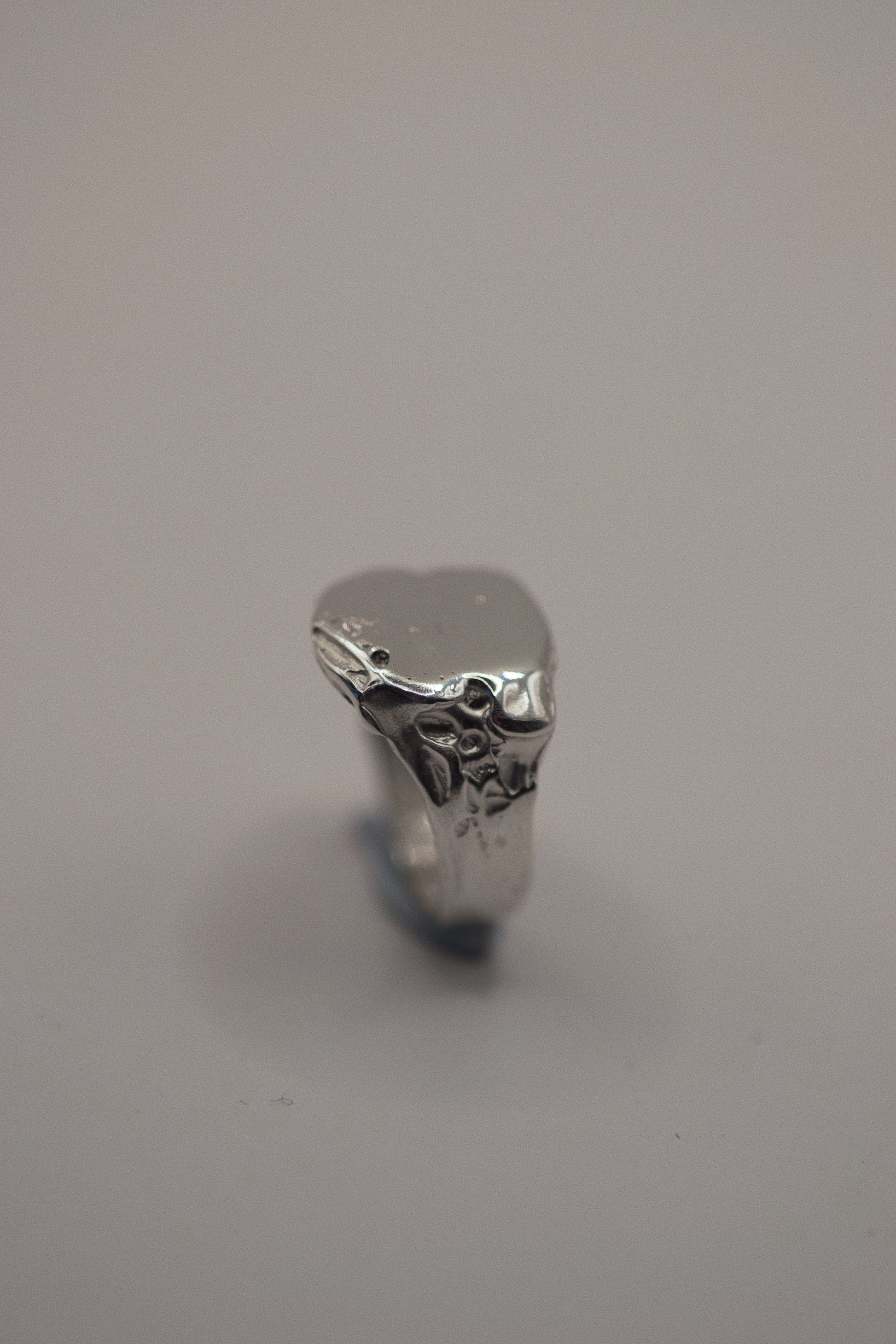 Handmade from solid 925 sterling silver, this signet ring is marked by organic dips and grooves that provide a textured, rugged finish. The smooth band of the ring leads to an intentionally uneven surface, where the dips and craters add character and depth. The silver’s natural imperfections make it a striking piece, offering an earthy look that’s refined yet grunge-inspired. This ring is cast using the lost wax method, making it a one-of-a-kind piece.