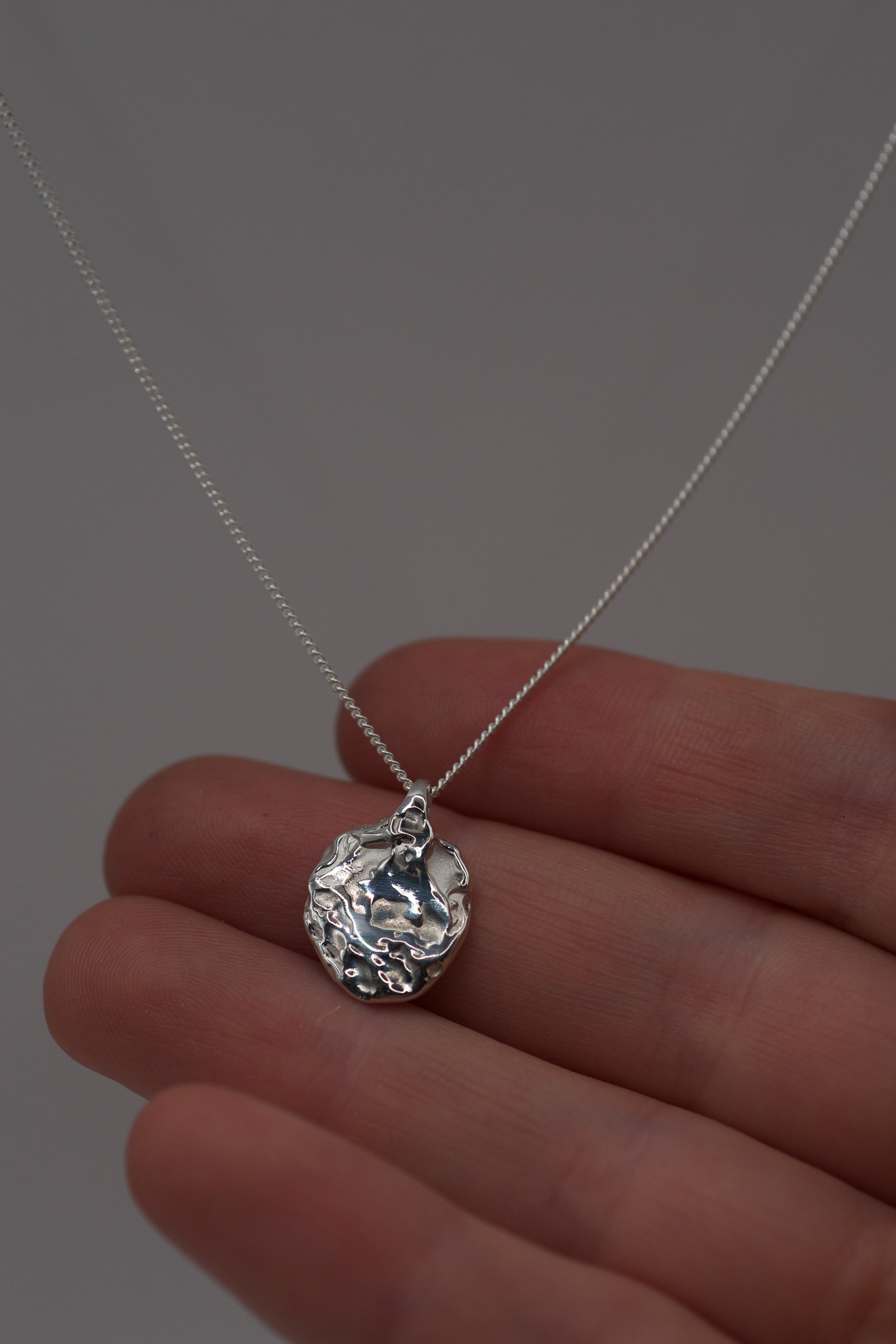 Organic molten 925 sterling silver pendant created using lost wax casting, shown hanging from a fine chain and resting against fingers.