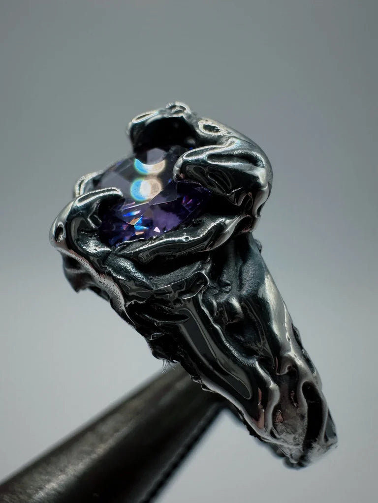 Featuring a molten metal sterling silver design, this ring boasts an amethyst centrepiece secured by three gothic claws. The intricate grooves and darkened details create a captivating look, enhanced by the organic texture achieved through the lost wax process.