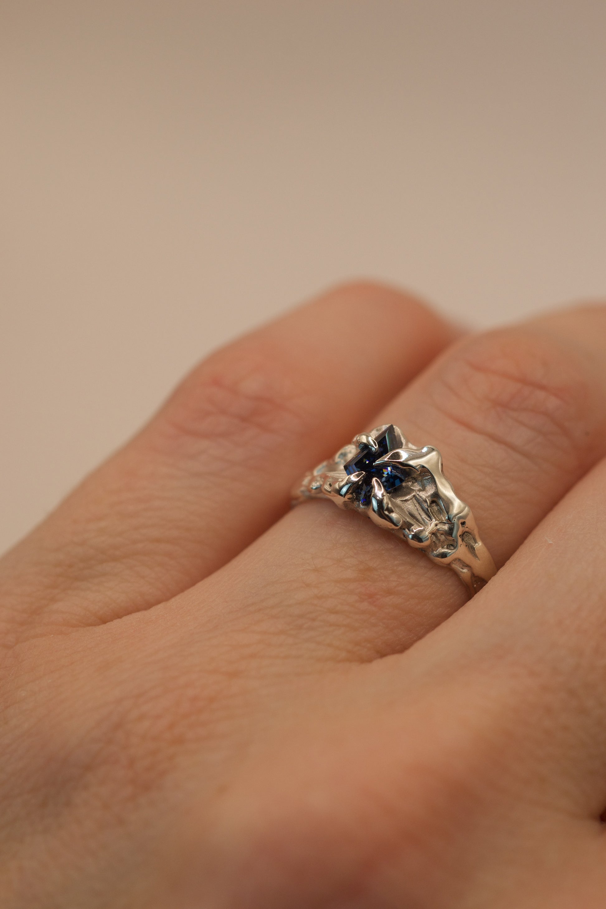 A unique asymmetrical engagement-style ring in 925 sterling silver, handmade with lost wax. The organic molten band holds a vivid blue kite cut moissanite in gothic inspired claws.