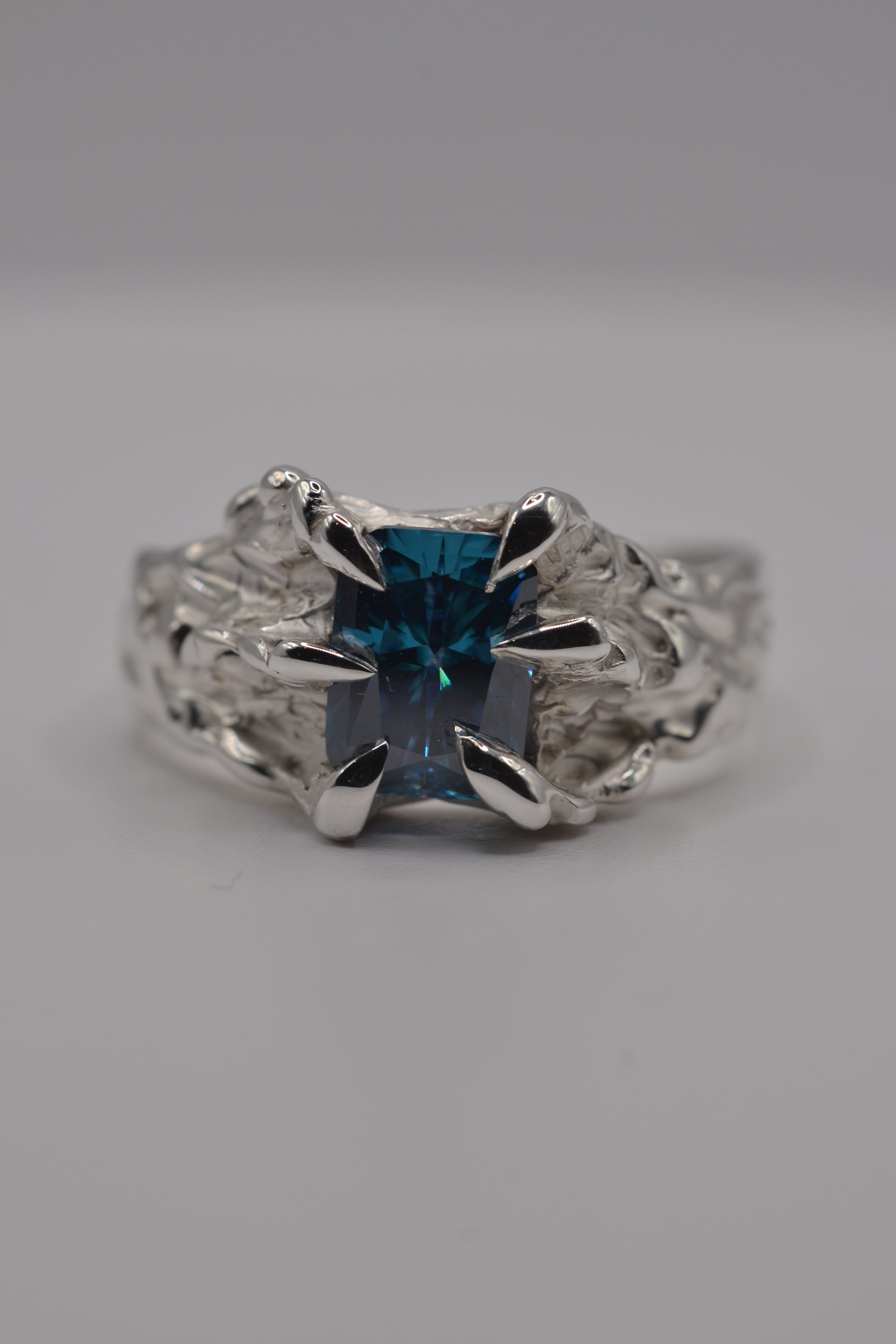 Textured alternative silver ring handcrafted using the lost wax casting technique, featuring a blue radiant cut moissanite.