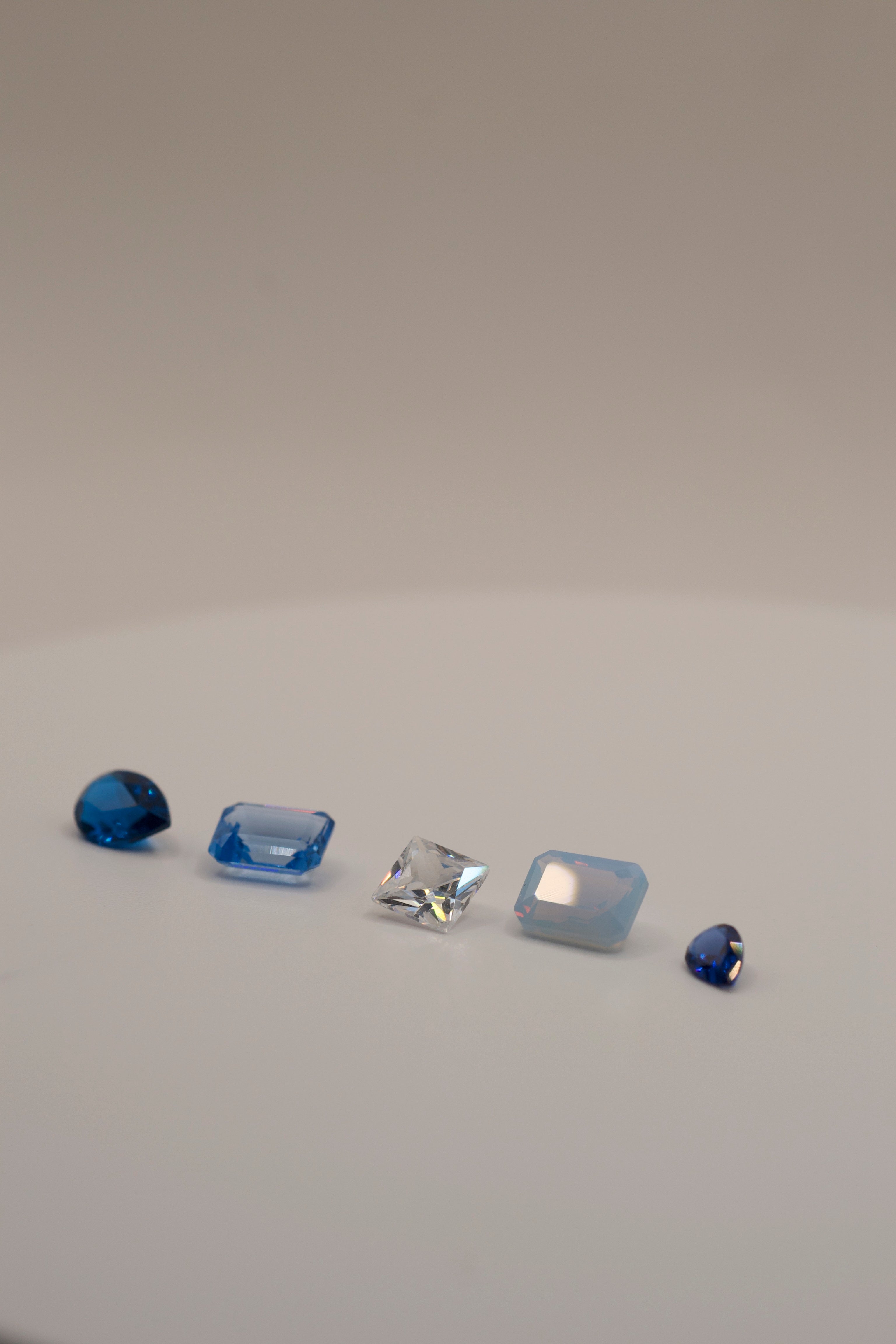 Cast in place gemstones for jewellery – assorted shapes and colours including pear cut blue, rectangular emerald cut light blue, radiant white CZ, rectangular opal nano crystal, and triangular royal blue gem. Lab-created ethical stones for lost wax casting.