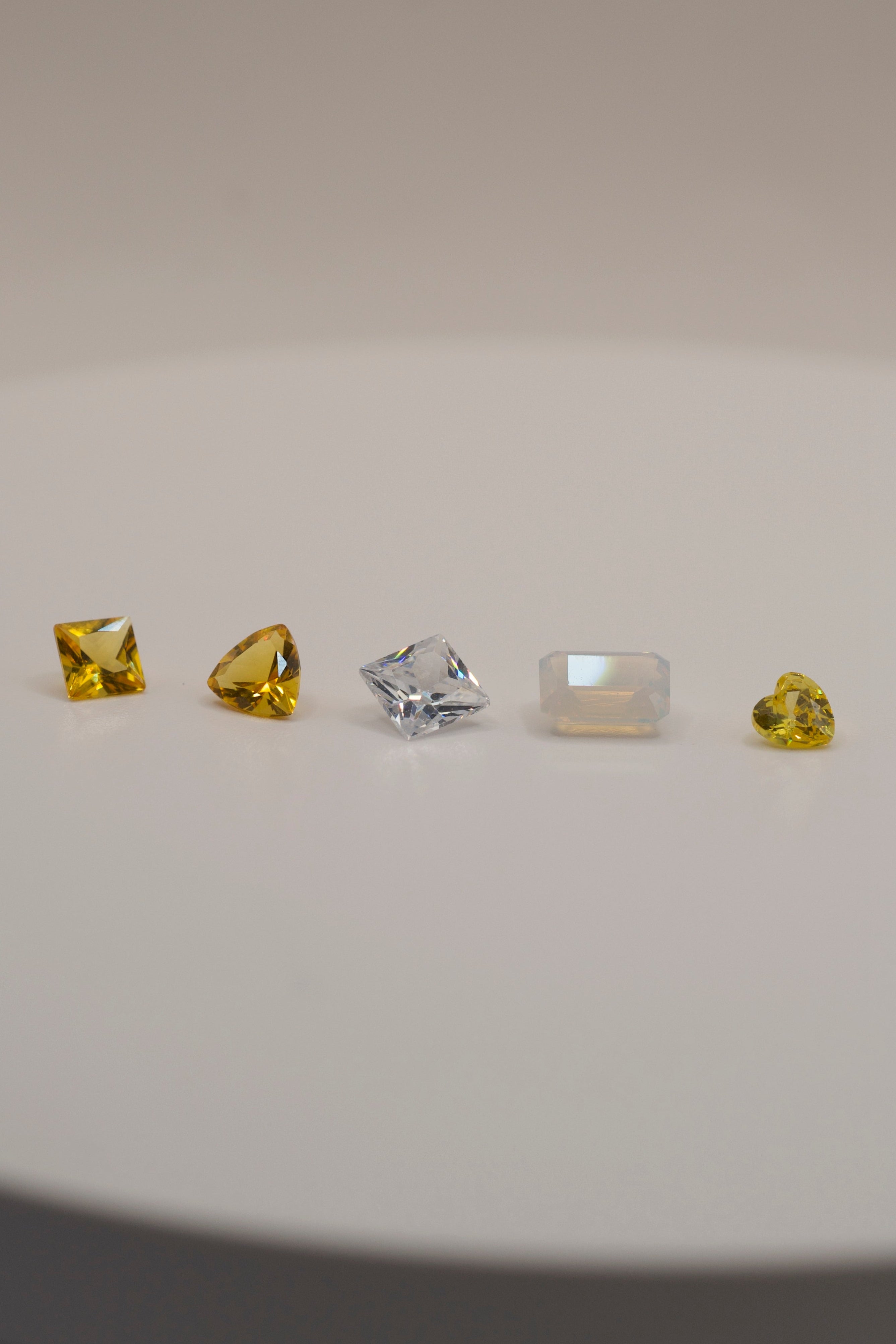 Gemstones for cast in place wax carving jewellery — yellow, clear, and opalescent faceted stones in unique cuts on a white background.