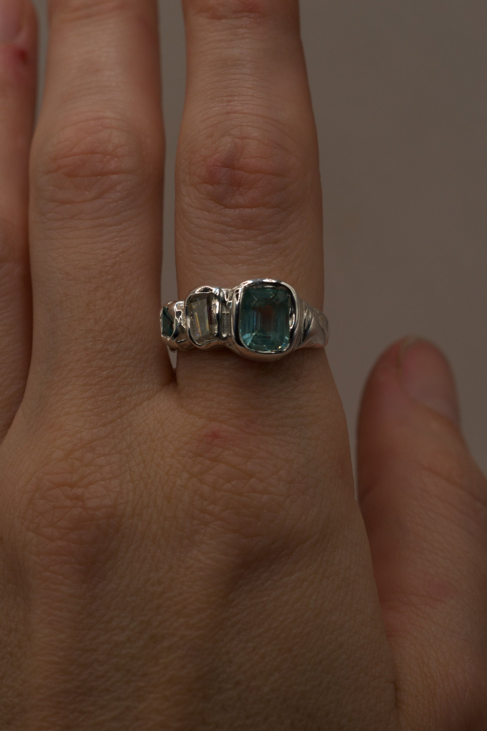 Hand-shot of an alternative organic sterling silver ring with molten design and high polish shine, featuring seafoam green gemstone, moissanite, and a green crystal, handmade with cast in place stones using the lost wax casting technique.