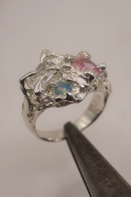 Handmade sterling silver ring with an emerald-cut clear white sapphire, pink cushion-cut cubic zirconia, and a round lab-grown aqua opal, cast using the lost wax method. The design features organic, molten textures in a fantasy-inspired floral arrangement.
