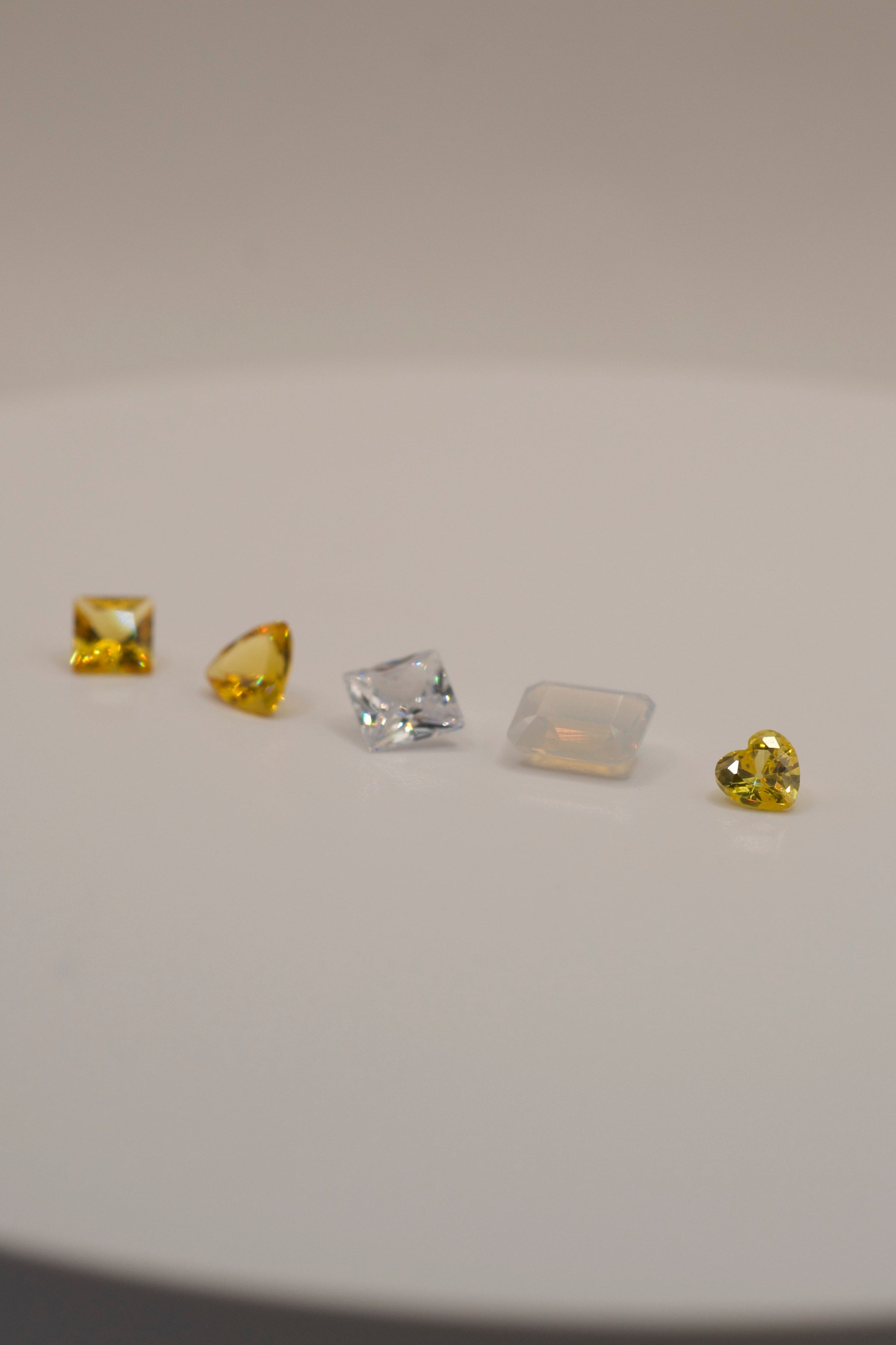 Assorted gemstones for lost wax carving and cast in place designs, including yellow square, triangular, clear princess cut, rectangular opal, and yellow heart cut.