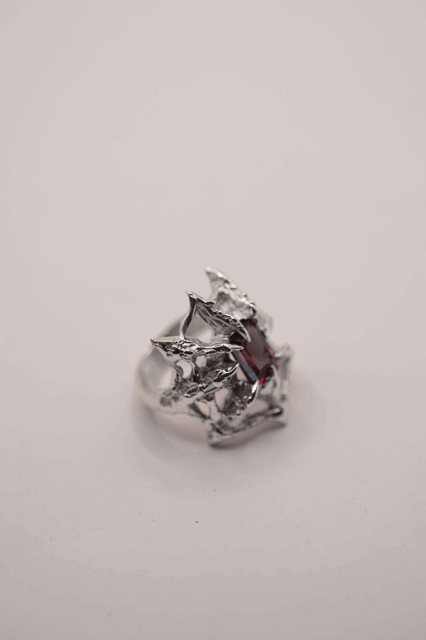 grunge gothic style lost wax cast sterling silver ring with a spider web holding a garnet emerald cut lab grown nano crystal. handcrafted using the lost wax method. 