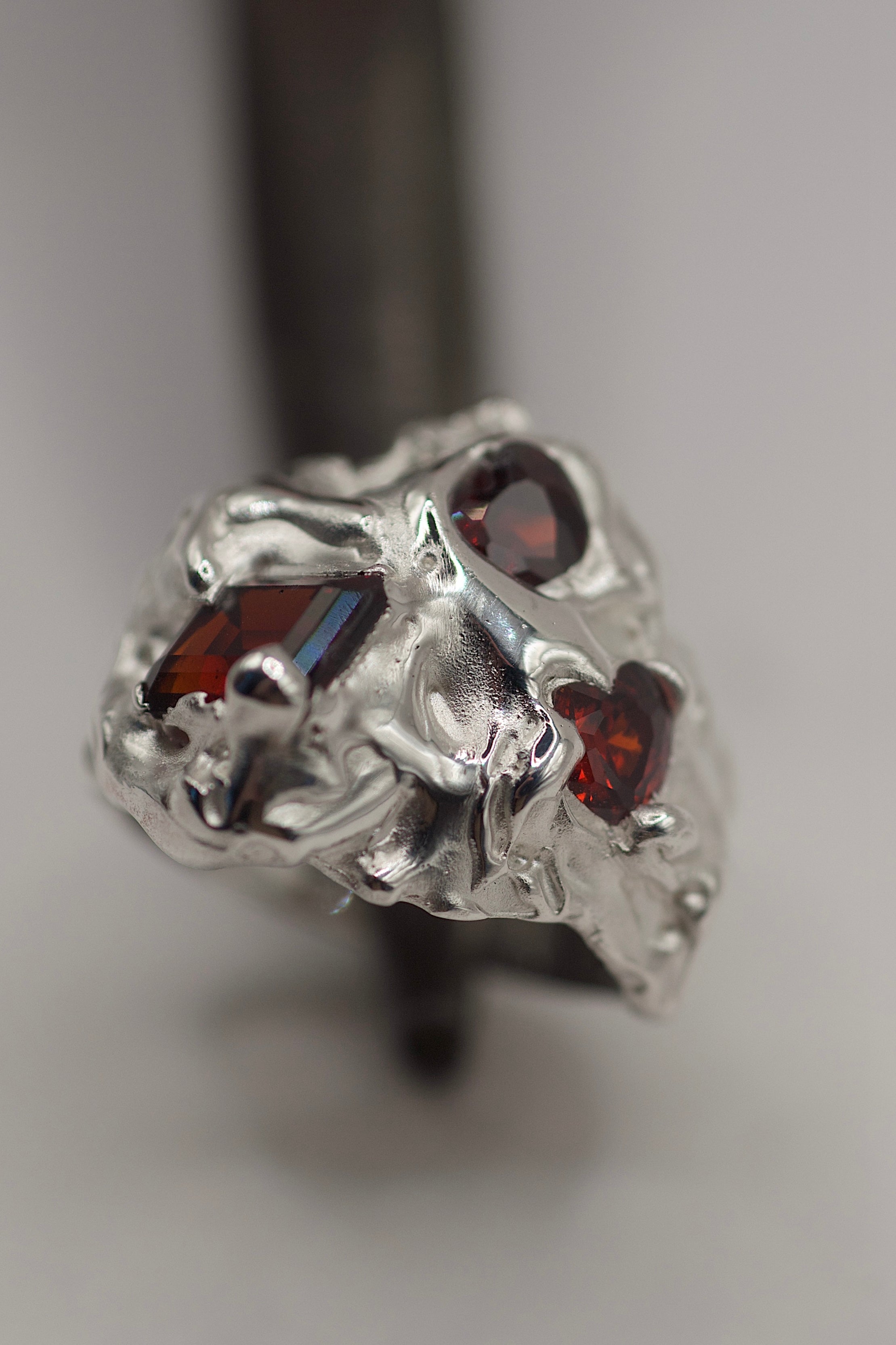 Close up of the Amour Ring showing red lab-grown garnet and red heart cubic zirconias within flowing organic molten sterling silver handmade using the lost wax technique