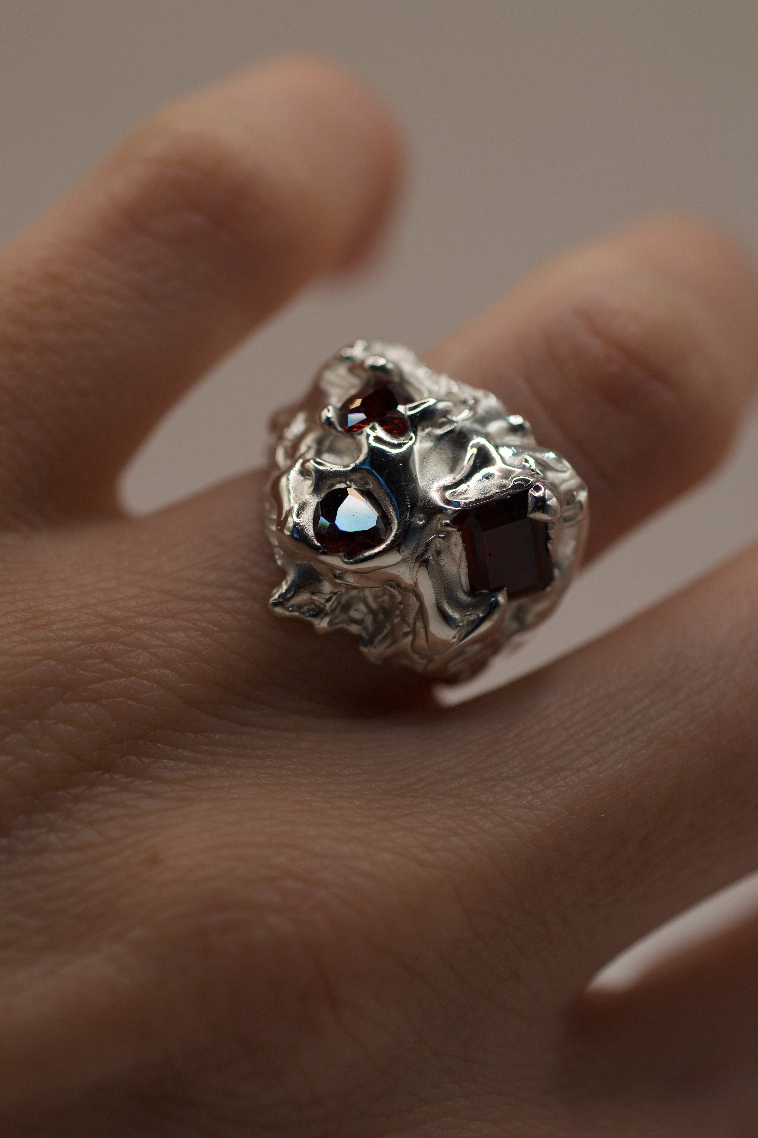 Lost wax cast silver Amour Ring worn on hand with red lab-grown garnet and heart cubic zirconia in organic molten silver setting