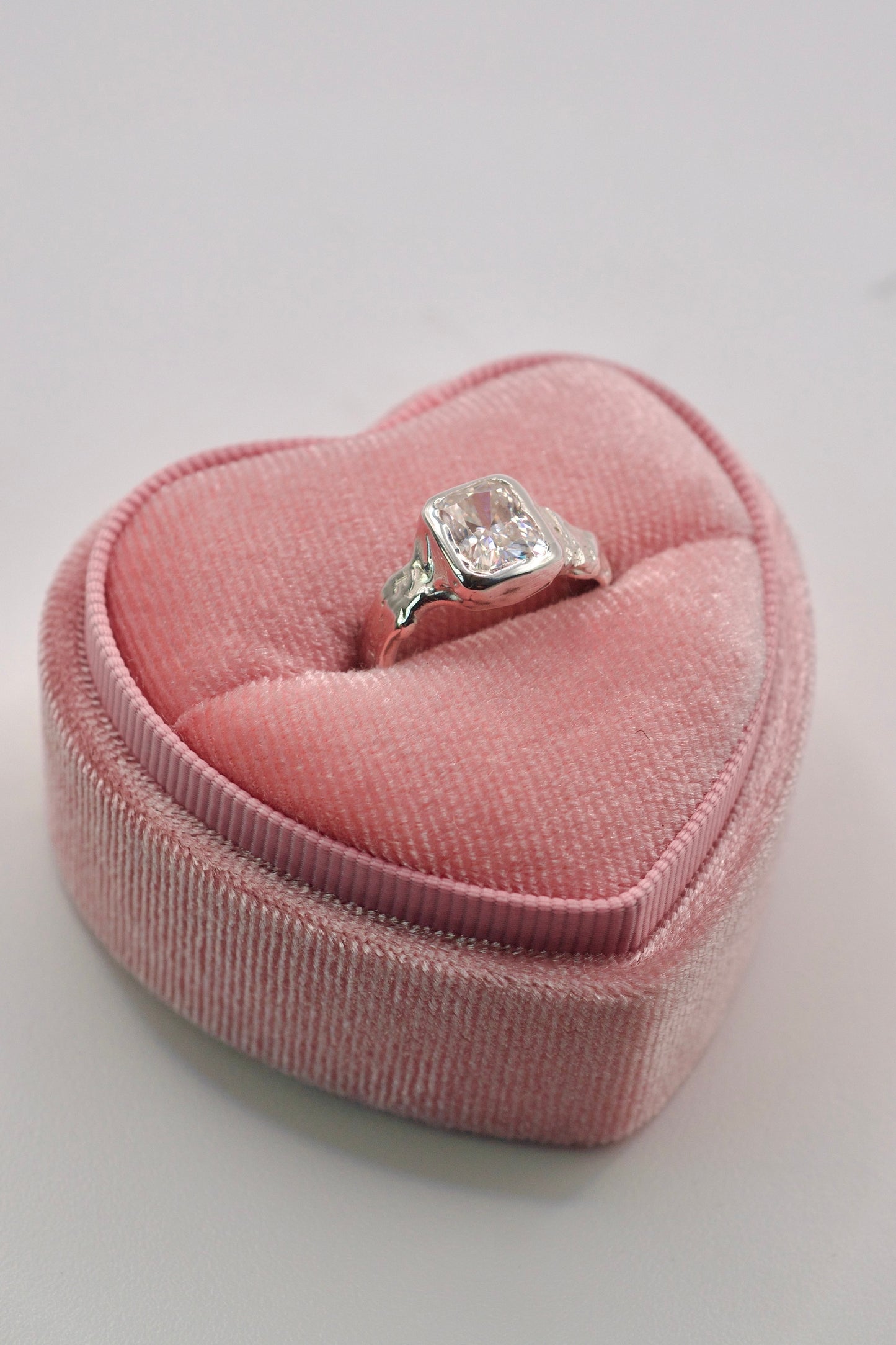 sterling silver organic ring with radiant cut white moissanite in bezel setting sitting in a pink velvet heart ring box