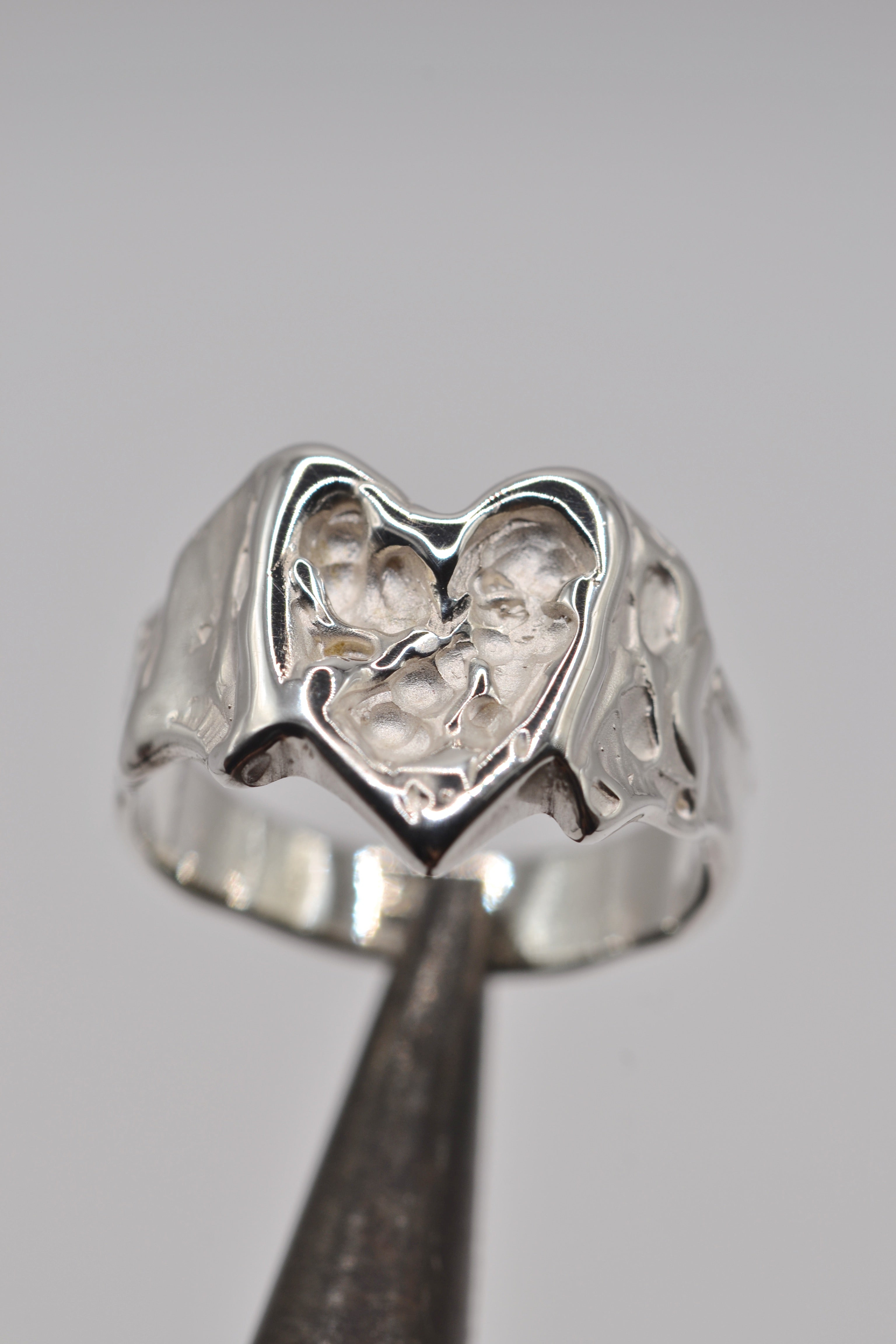 Angled view of the Bleeding Heart Ring held in tweezers showing organic sculpted sterling silver heart handmade using lost wax casting