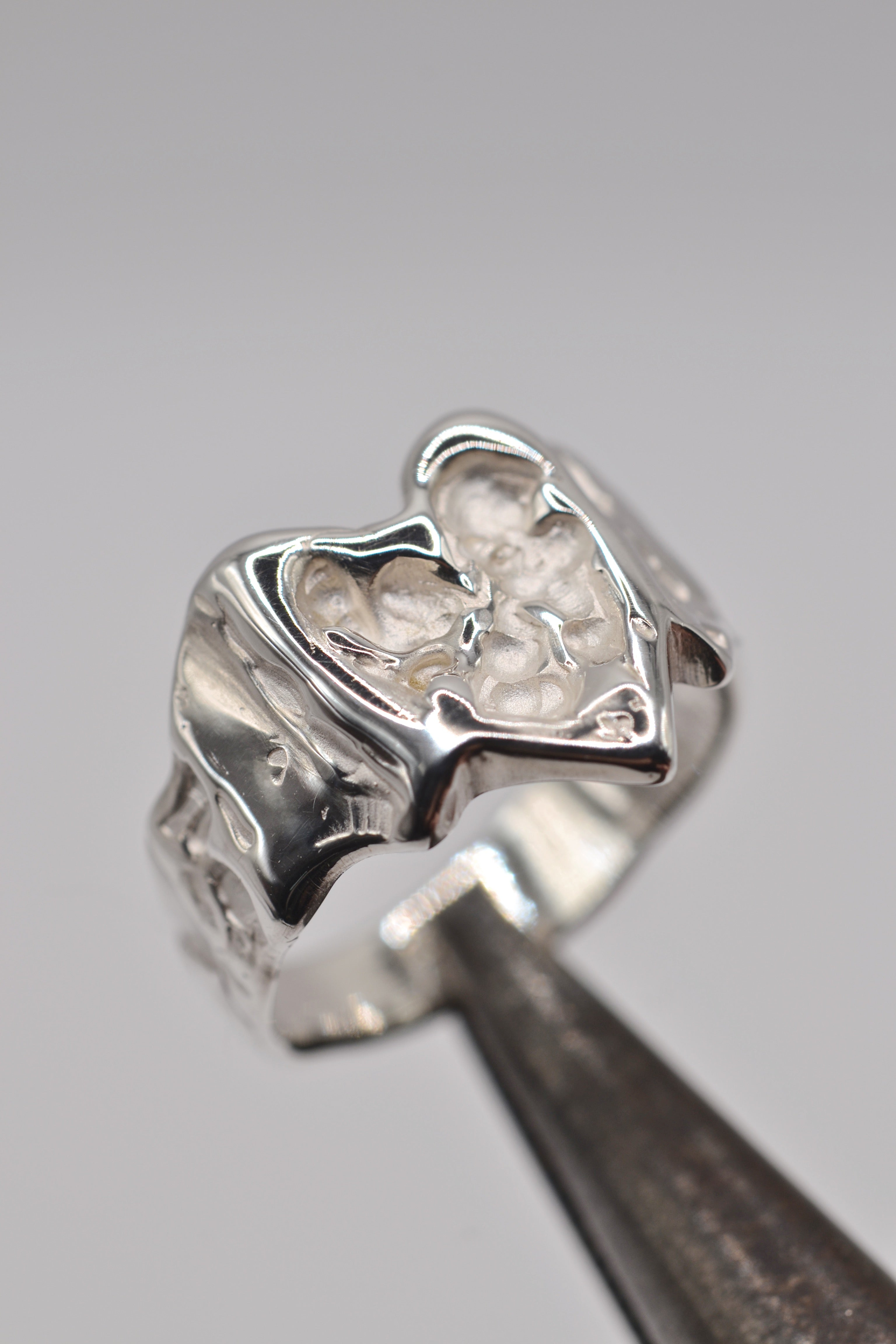 Bleeding Heart Ring held in tweezers showing sculpted sterling silver heart and flowing vein detail handmade using the lost wax casting technique