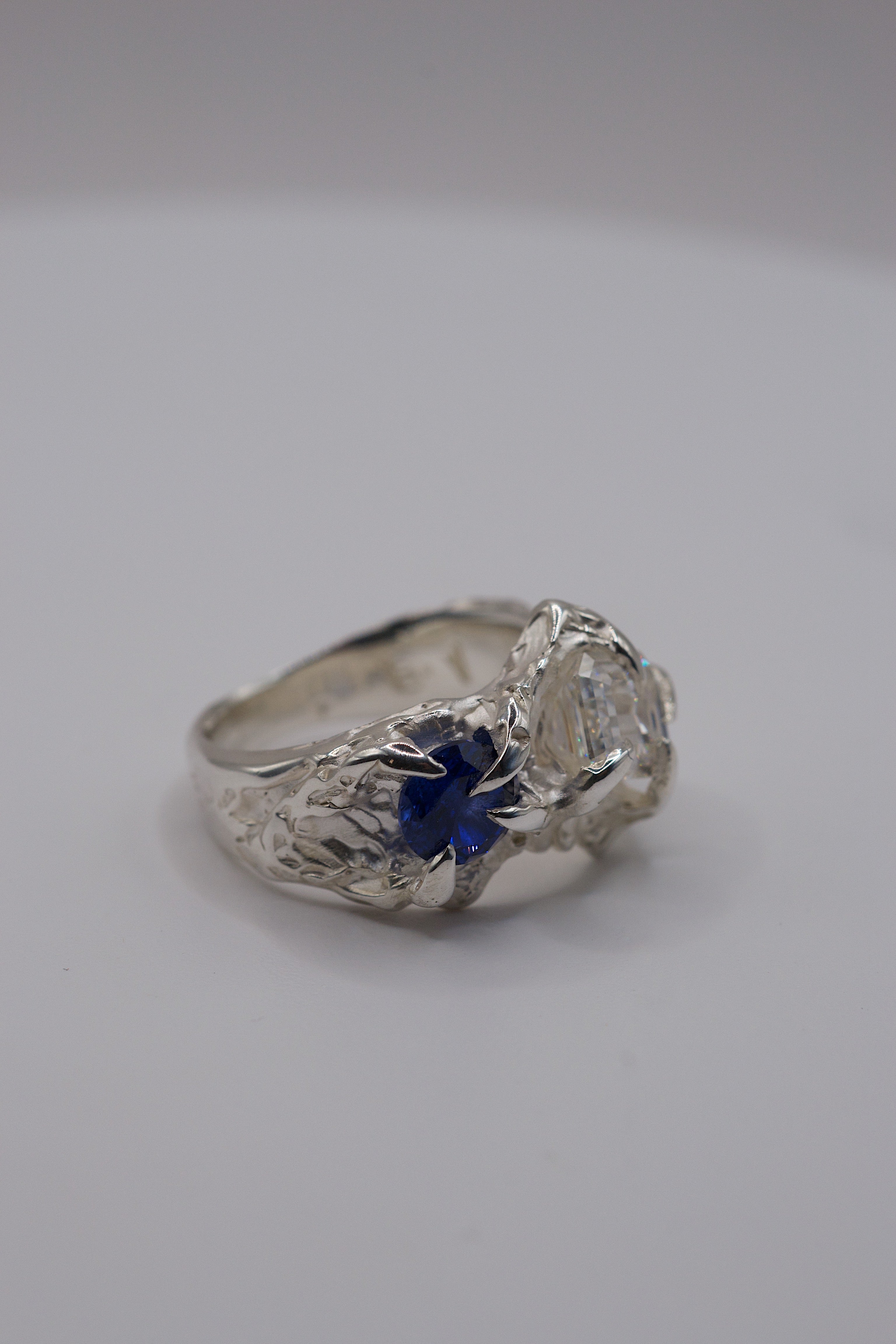 Flat view of the Blue Crush Ring showing organic recycled sterling silver band and blue sapphire with moissanite setting handmade using lost wax casting