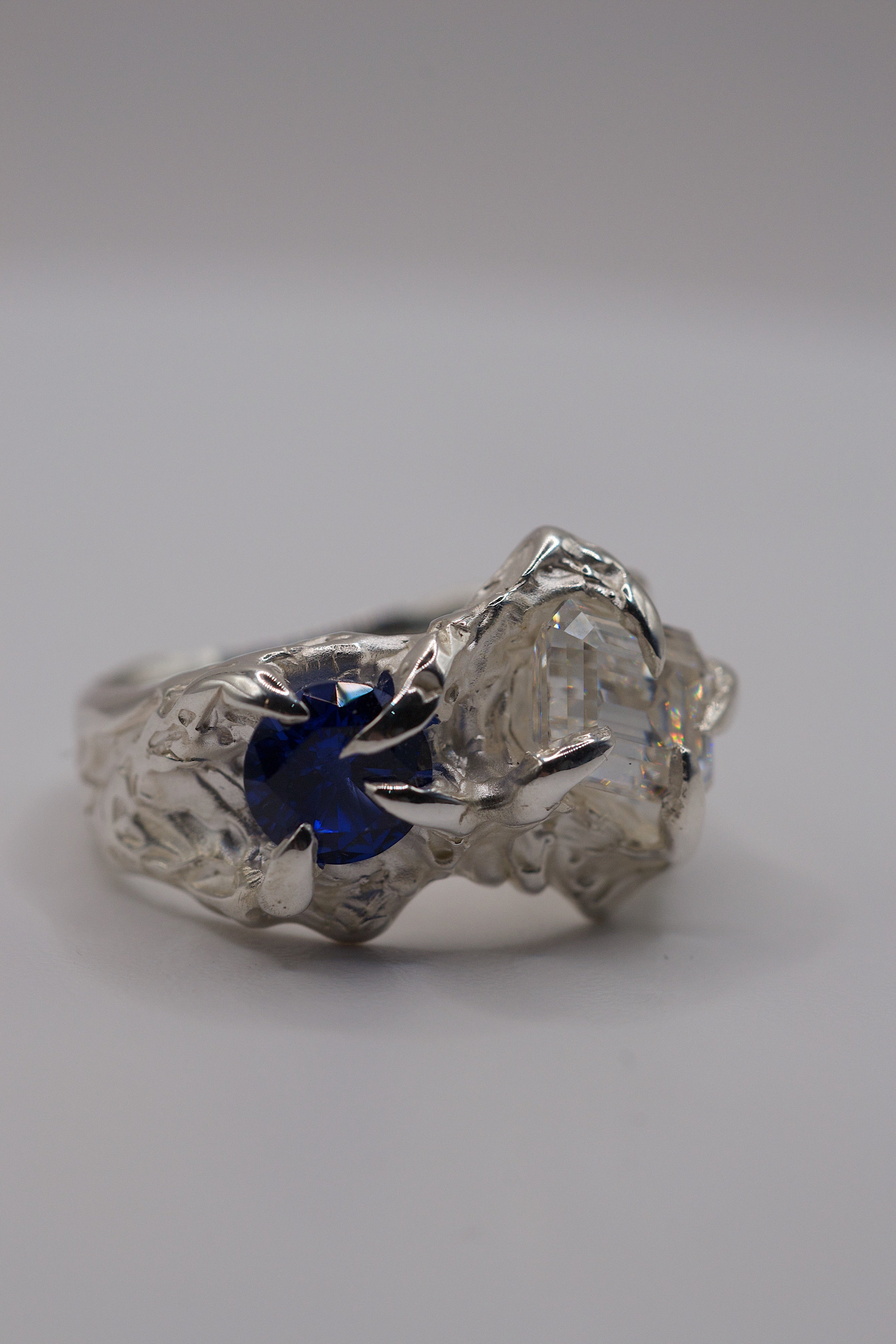 Angled view of the Blue Crush Ring showing natural blue sapphire and white moissanite within organic molten sterling silver handmade using lost wax casting