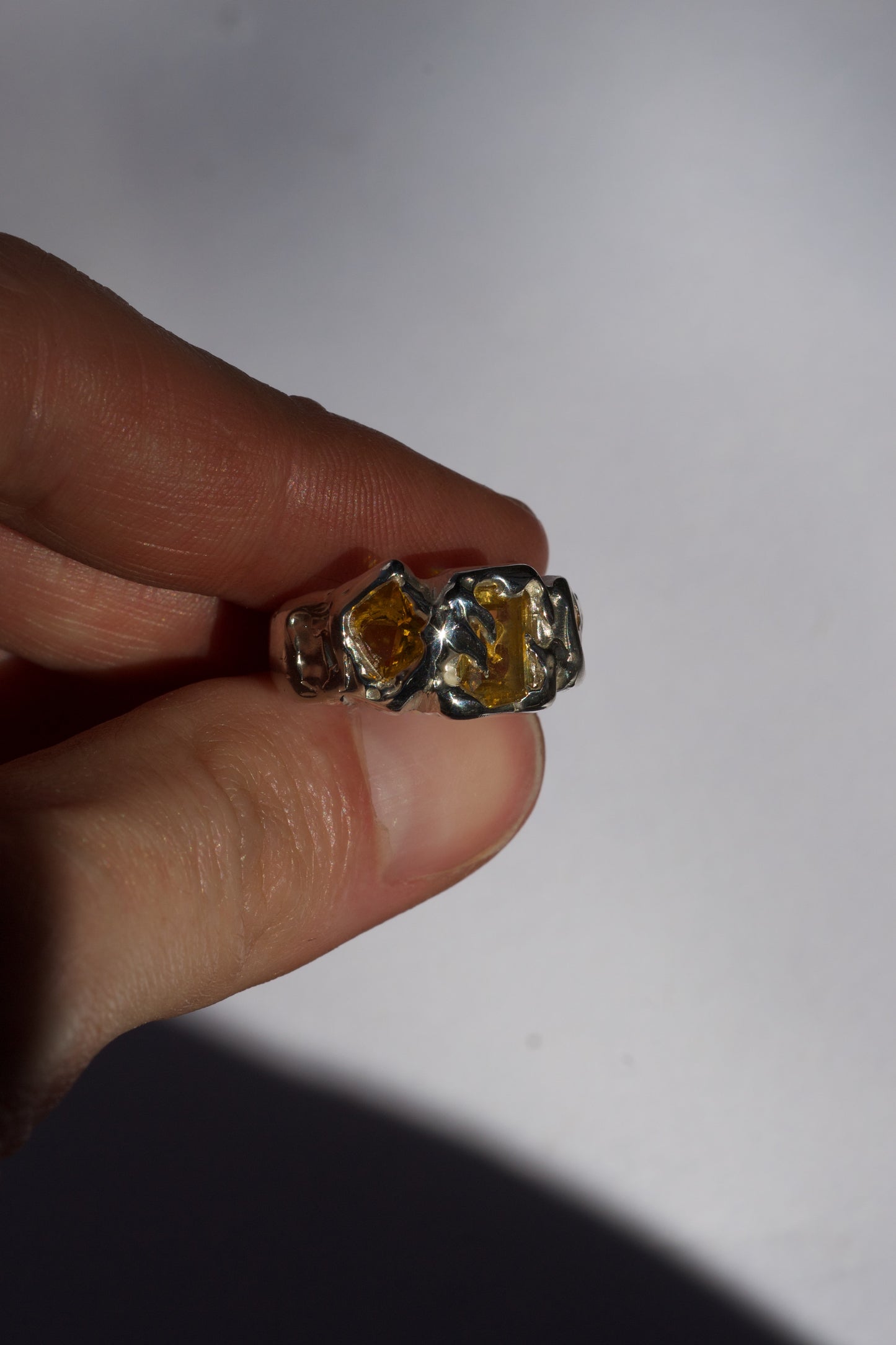 Hand holding a silver ring with a large yellow emerald-cut gemstone against a white background
