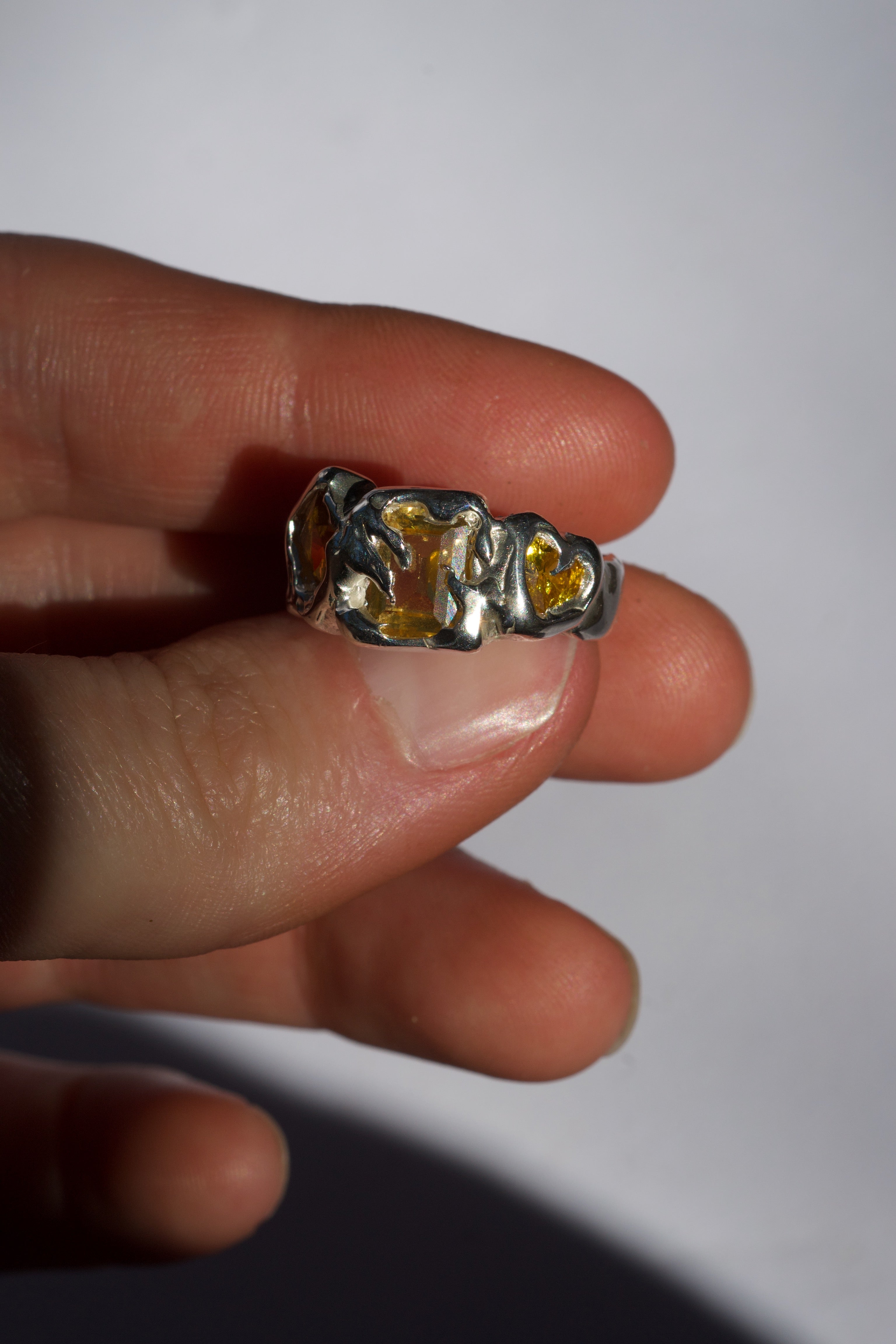 Molten silver lost wax ring with yellow gemstones held on a finger against a white background