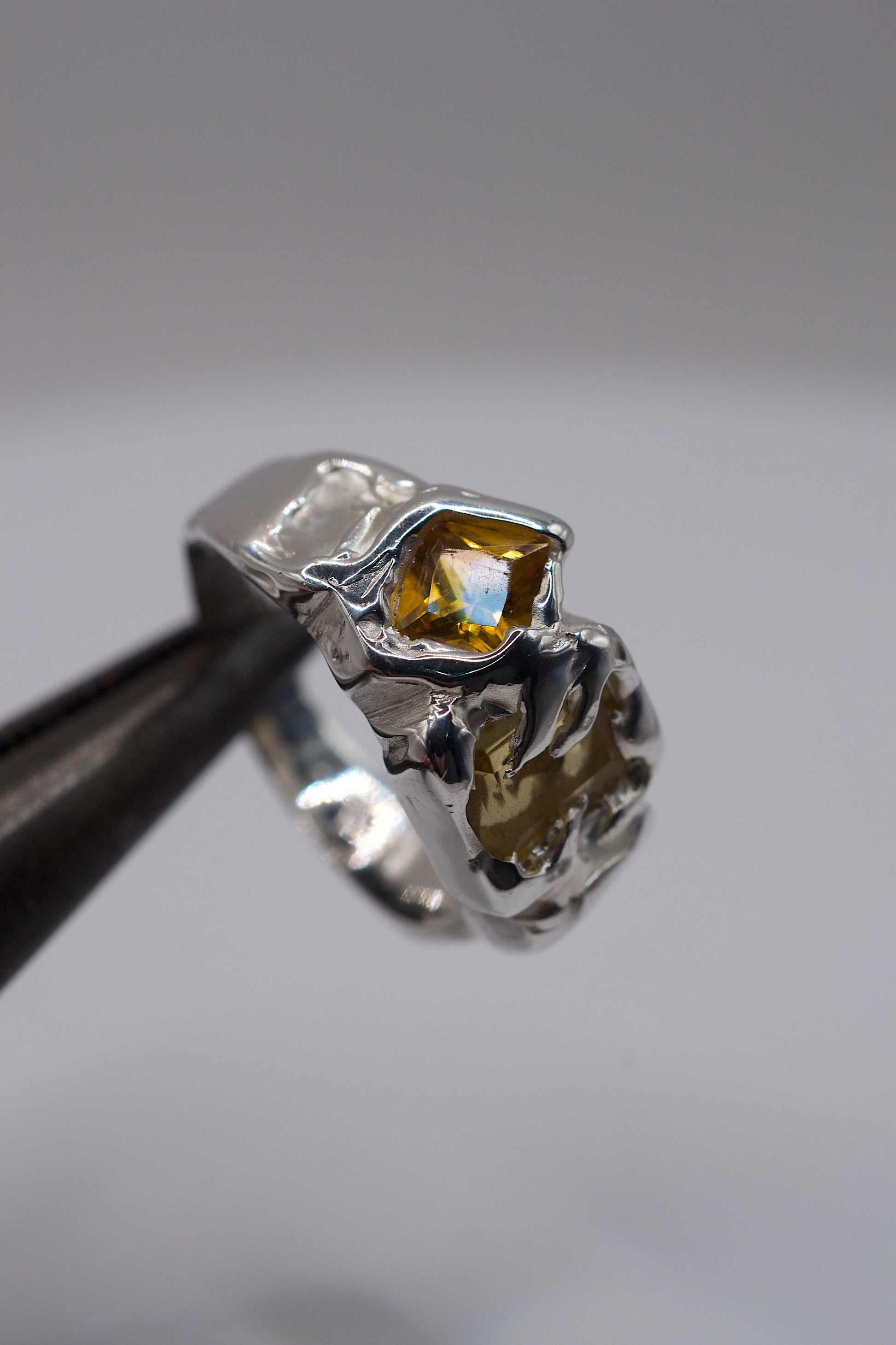 Handmade organic silver alternative ring with a yellow gemstone held by tweezers on a white background