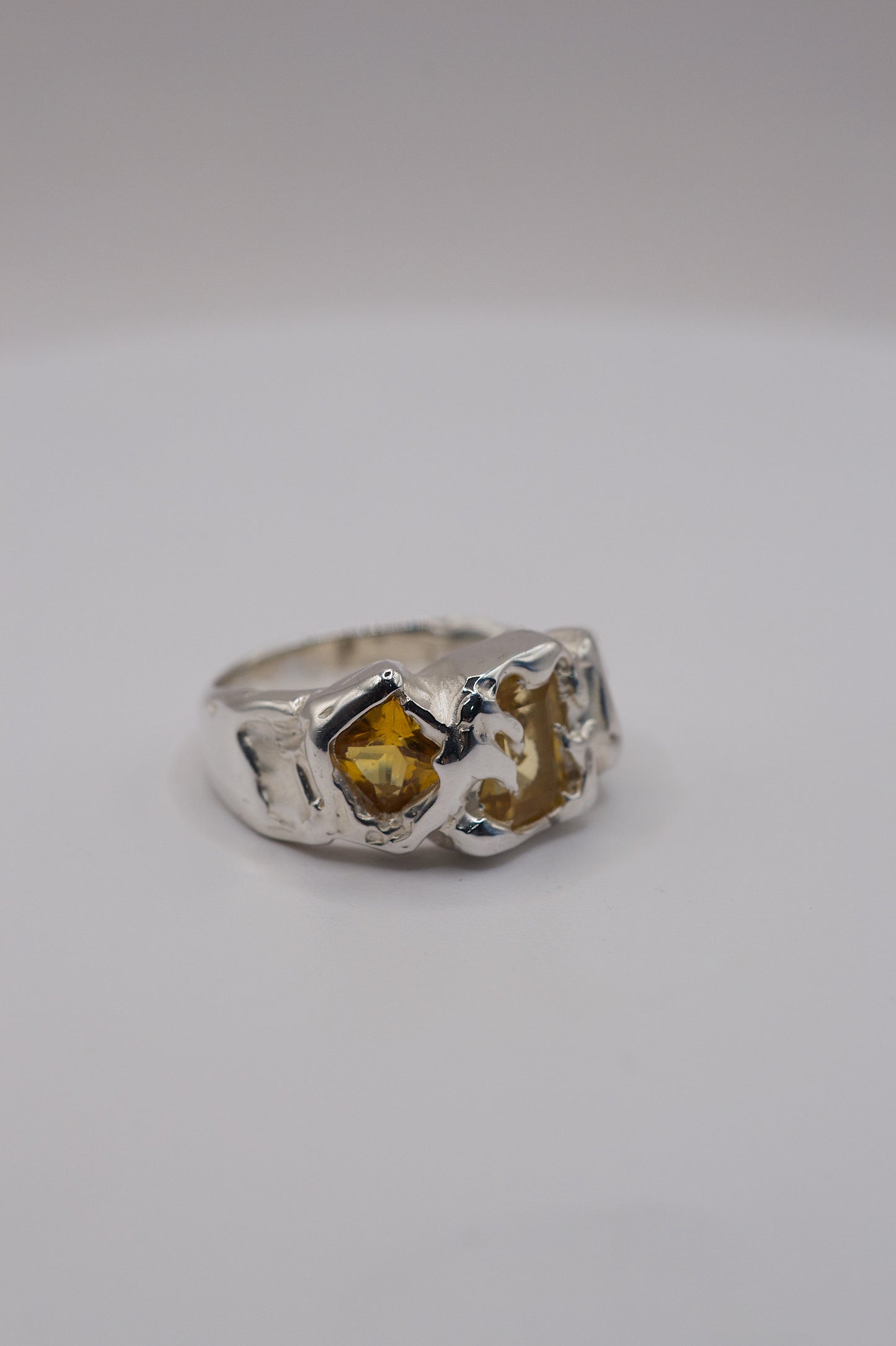 Molten silver unique ring with a yellow princess-cut gemstone on a white background