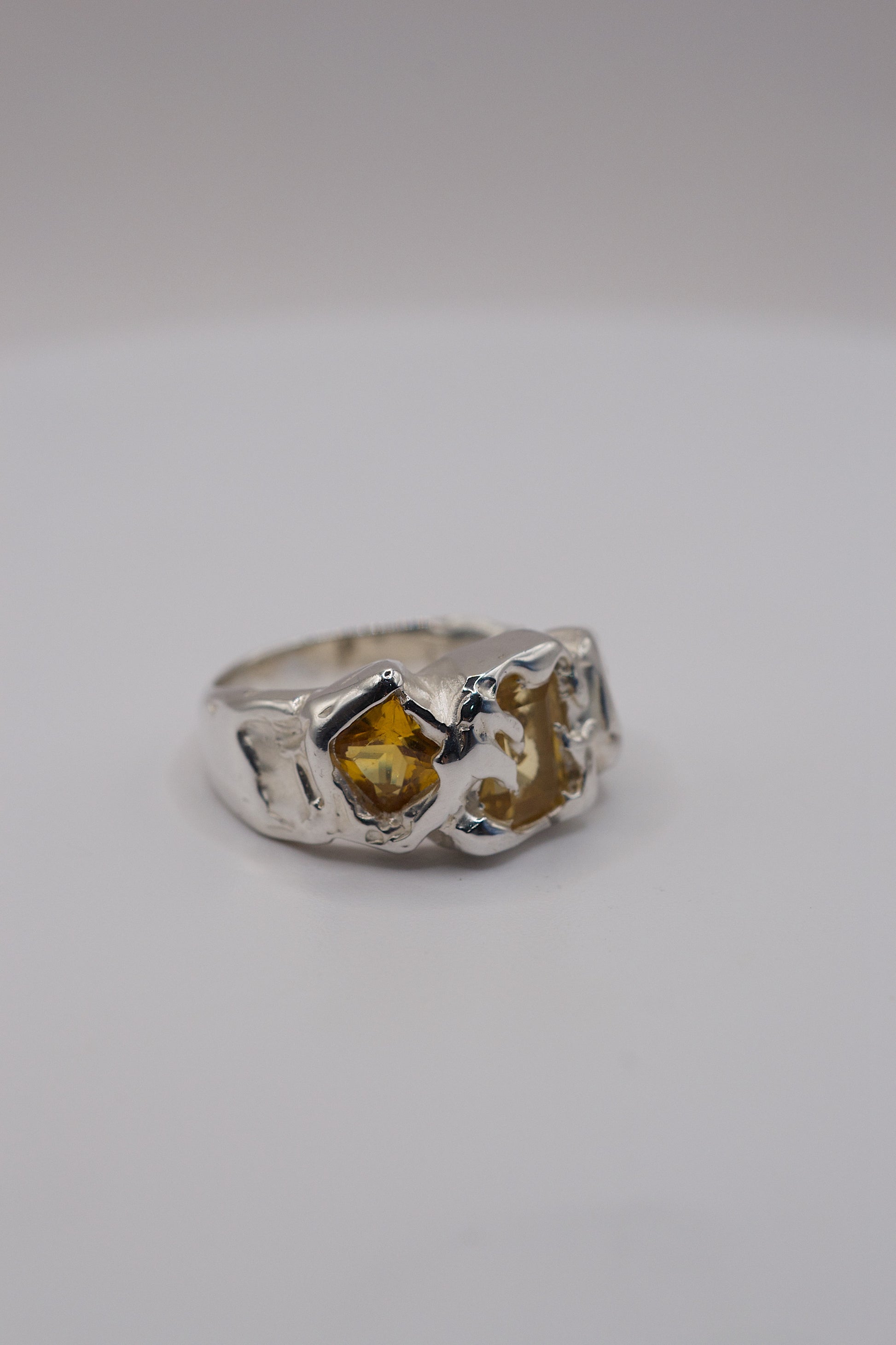 Molten silver unique ring with a yellow princess-cut gemstone on a white background
