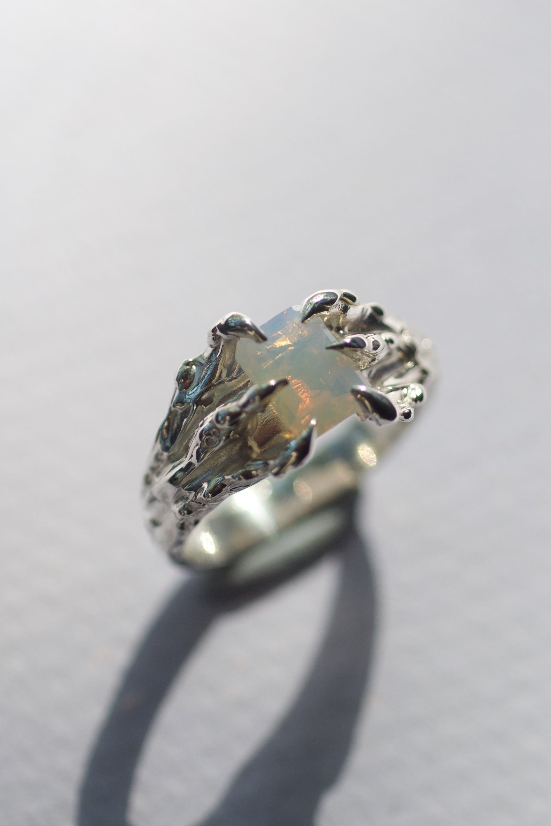 Handmade lost wax cast silver ring with molten dragon claws gripping a lab-grown opal crystal, alternative engagement ring sculpted using the wax carving technique