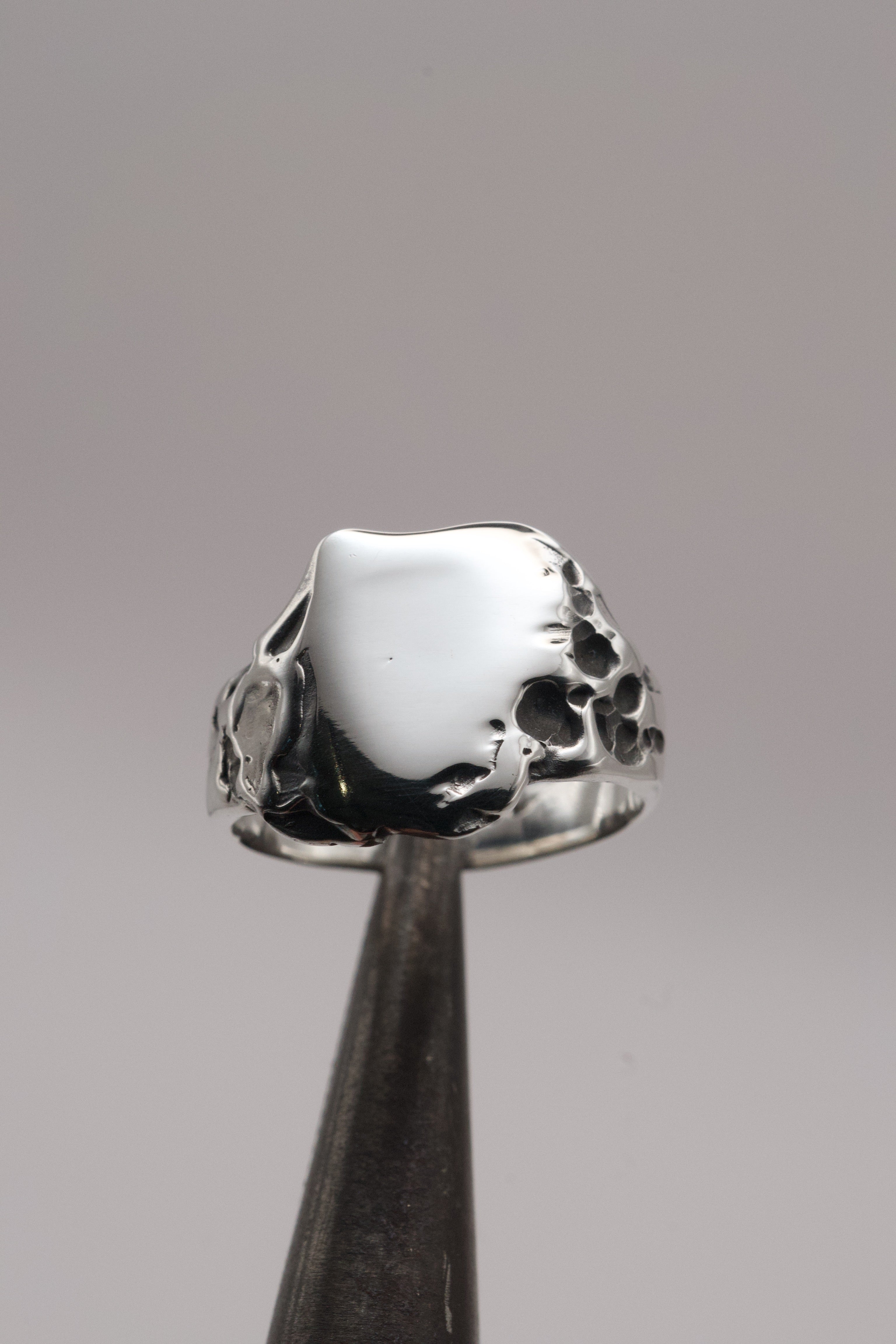 Duality Ring held in tweezers showing darkened sterling silver patina and dimensional organic molten texture handmade using the lost wax technique