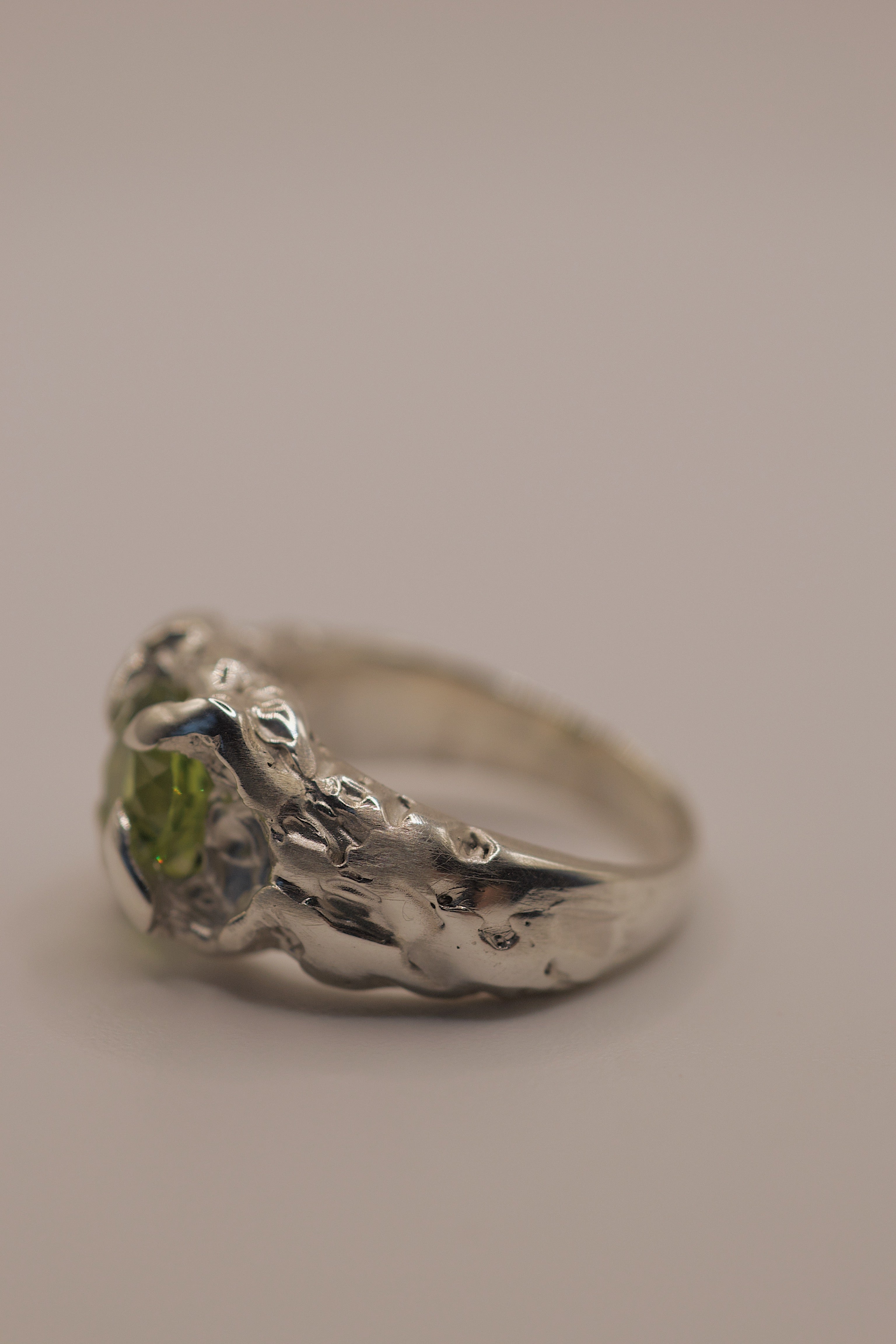 Flat angle of the Fern Ring showing organic flowing recycled sterling silver band and cushion cut green peridot lost wax cast