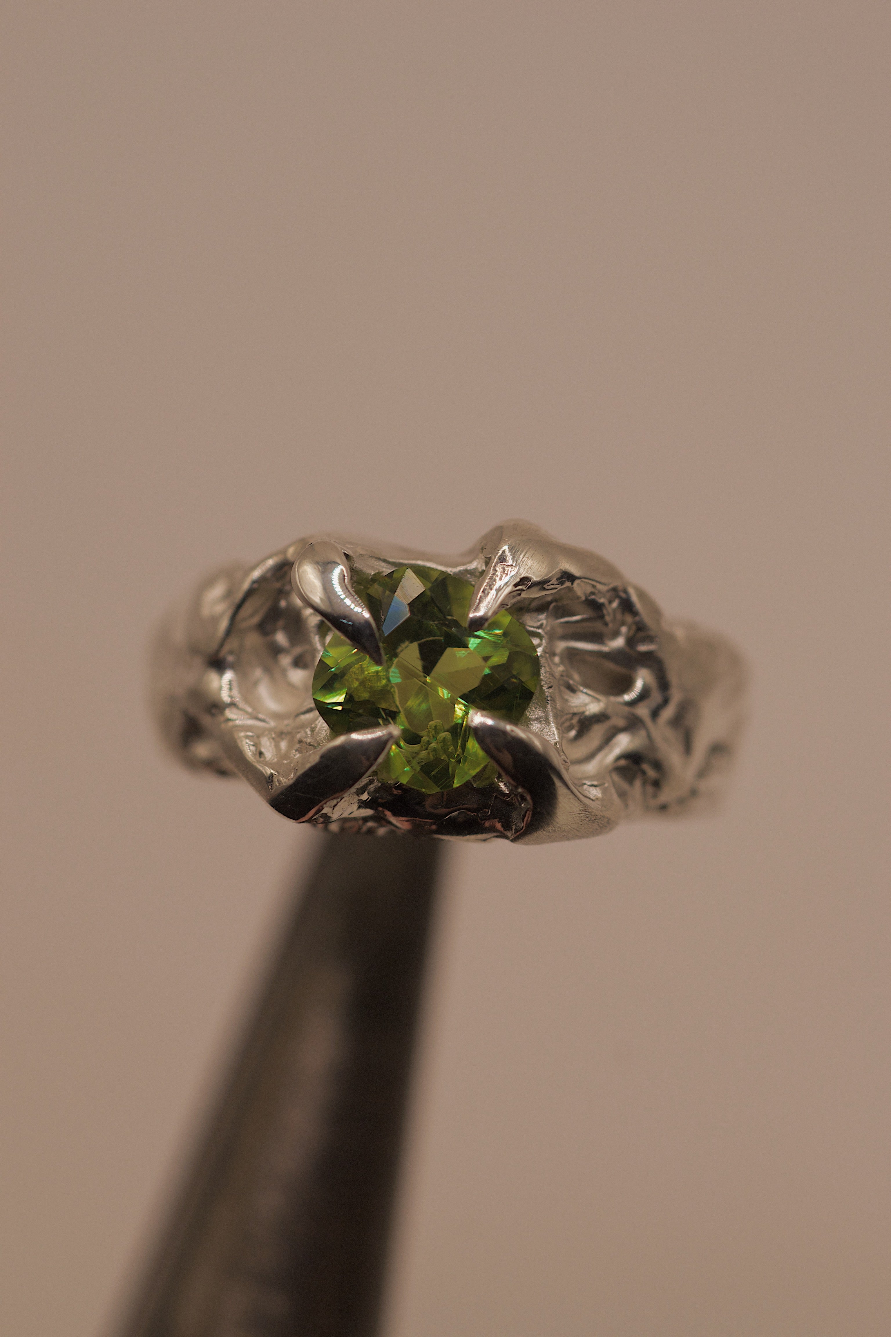 Fern Ring held in tweezers showing cushion cut lab-grown peridot within enchanting organic molten sterling silver handmade using the lost wax technique
