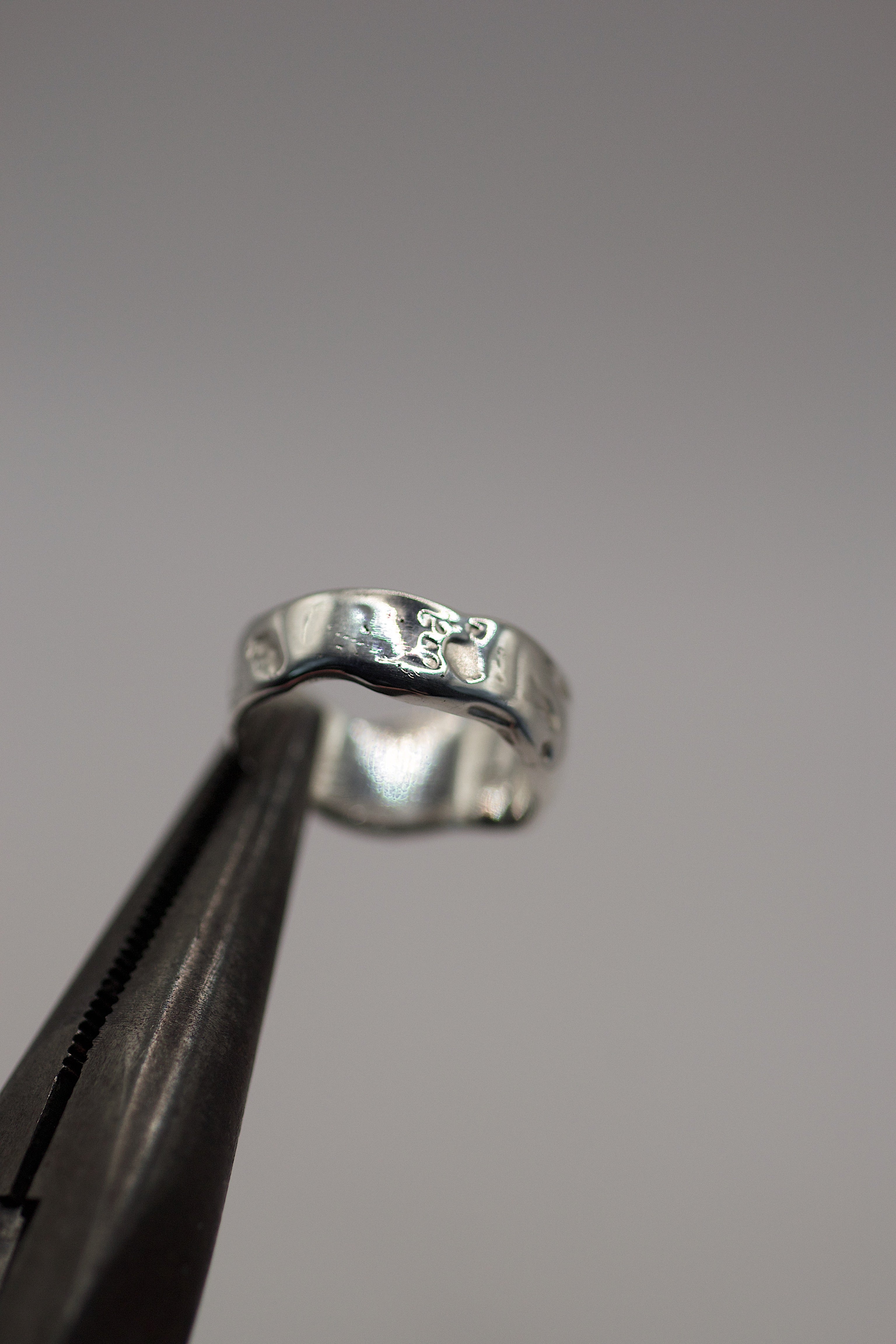 Molten Ring held in tweezers showing organic flowing sterling silver band with molten texture handmade using the lost wax casting technique