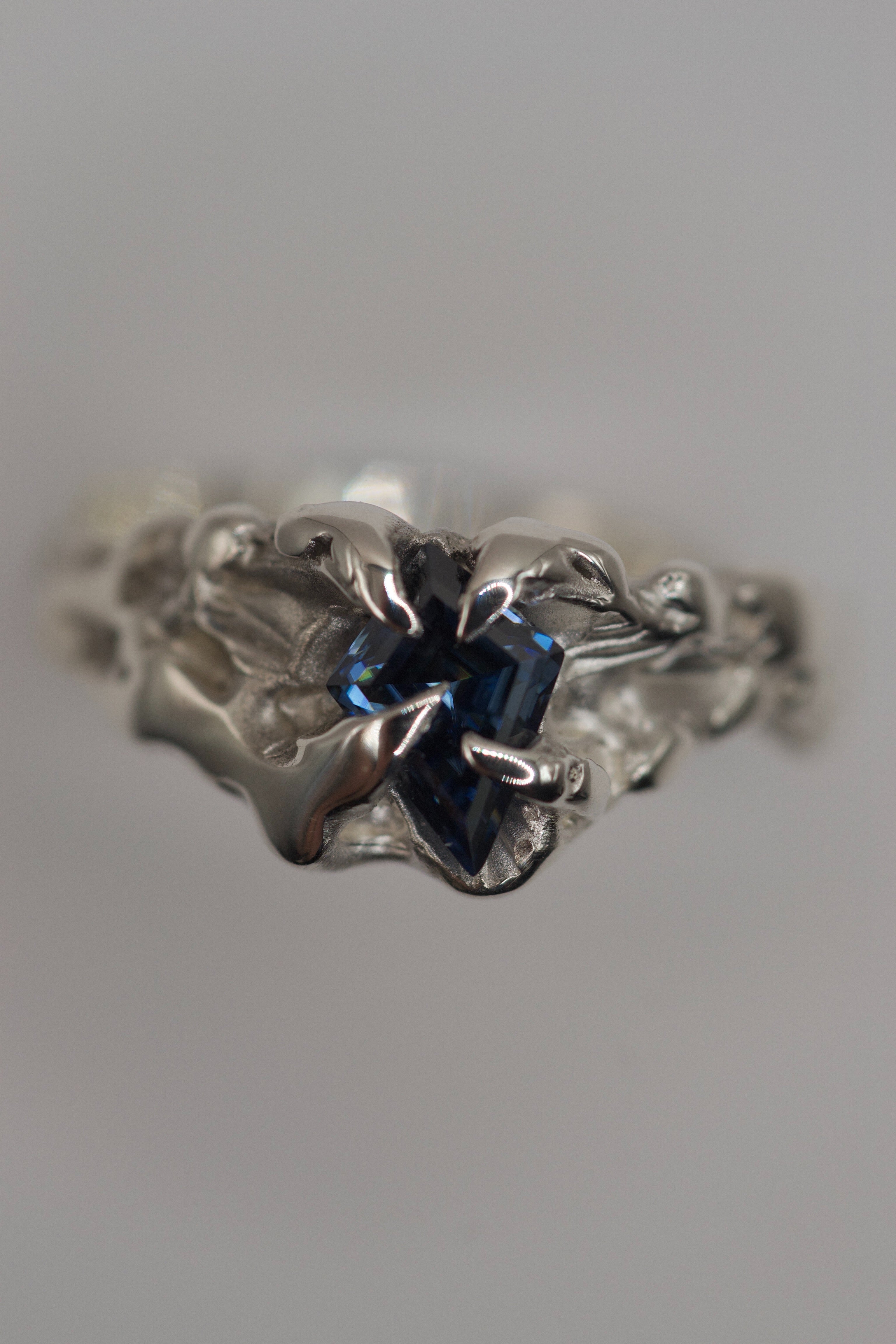 Handmade lost wax cast sterling silver ring with four velvet-like claws holding a kite cut blue moissanite, moody sculptural alternative ring made using the wax carving technique