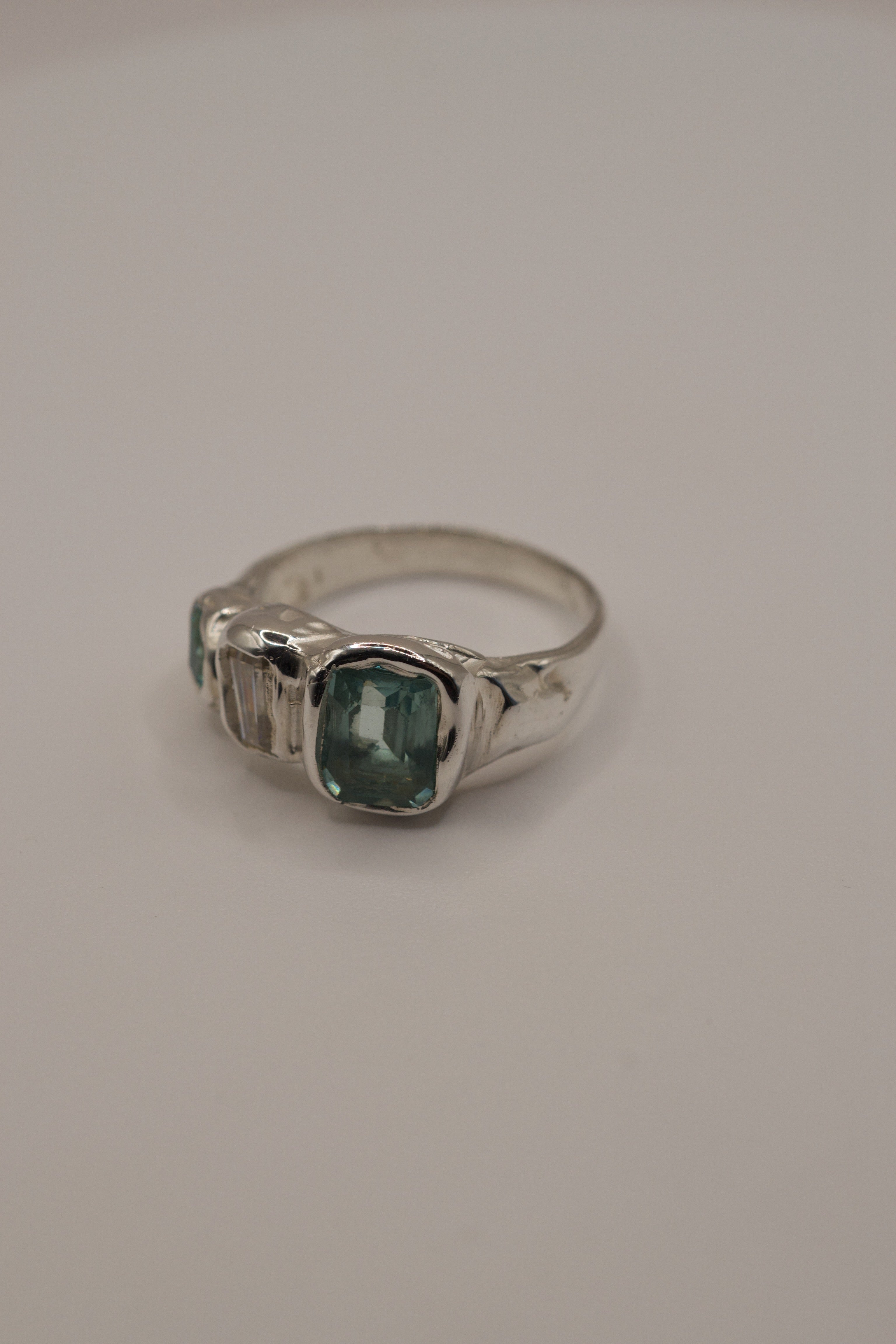 Organic molten 925 sterling silver ring with a high polish finish, featuring a central square-cut seafoam green gemstone, baguette-cut sparkling moissanite, and an additional green-toned crystal, handmade with cast in place gemstones using the lost wax casting process.