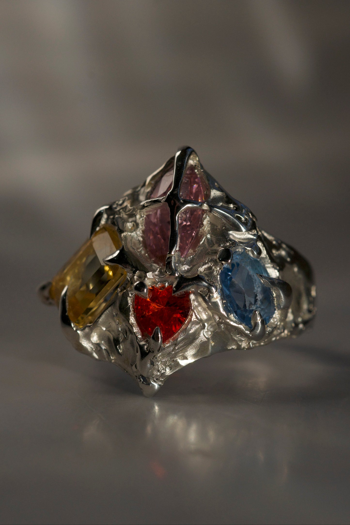 Silver ring with colorful gemstones on a gray background. Organic gothic style claw ring with multiple gemstones handmade with lost wax