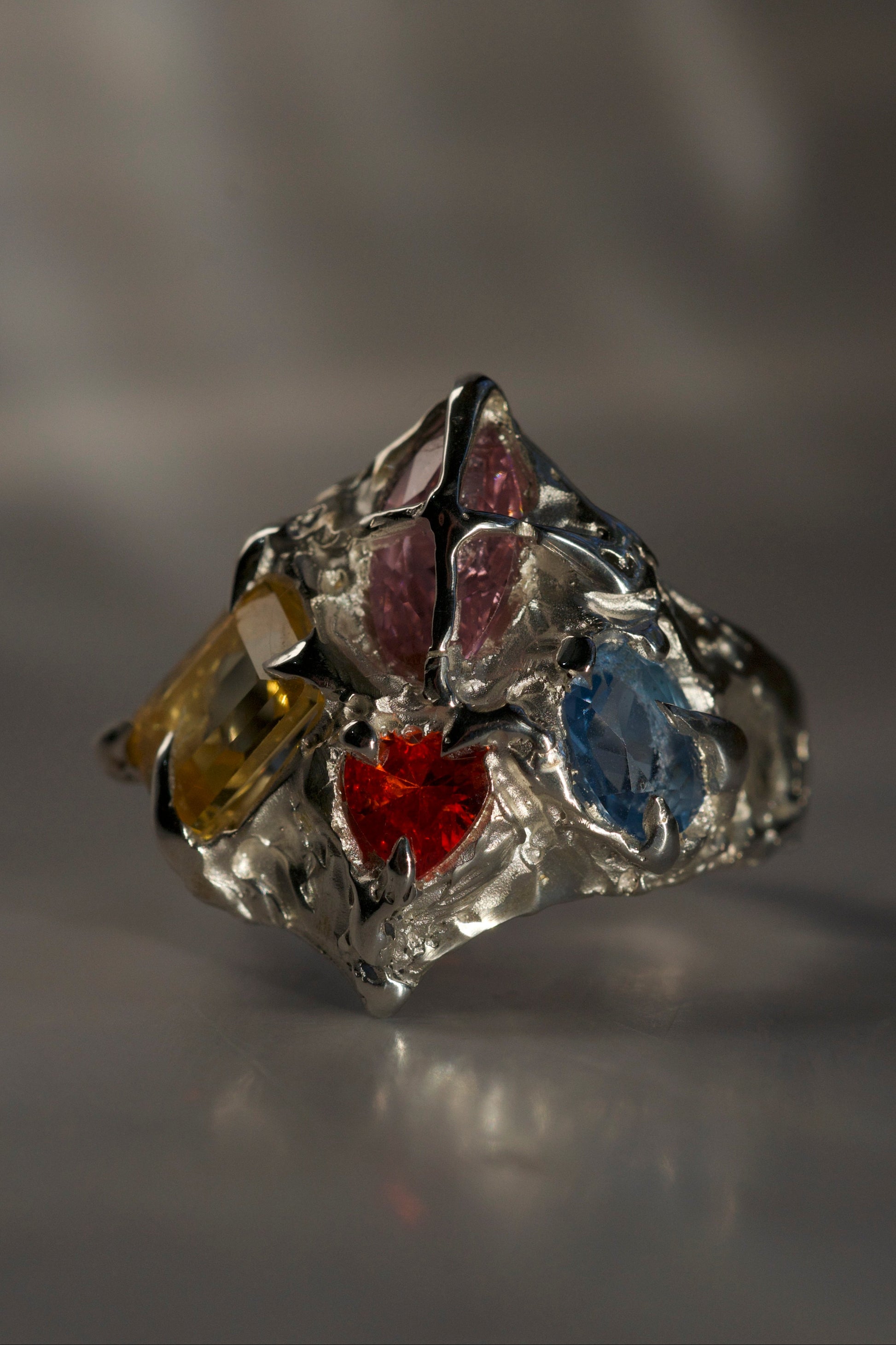 Silver ring with colorful gemstones on a gray background. Organic gothic style claw ring with multiple gemstones handmade with lost wax