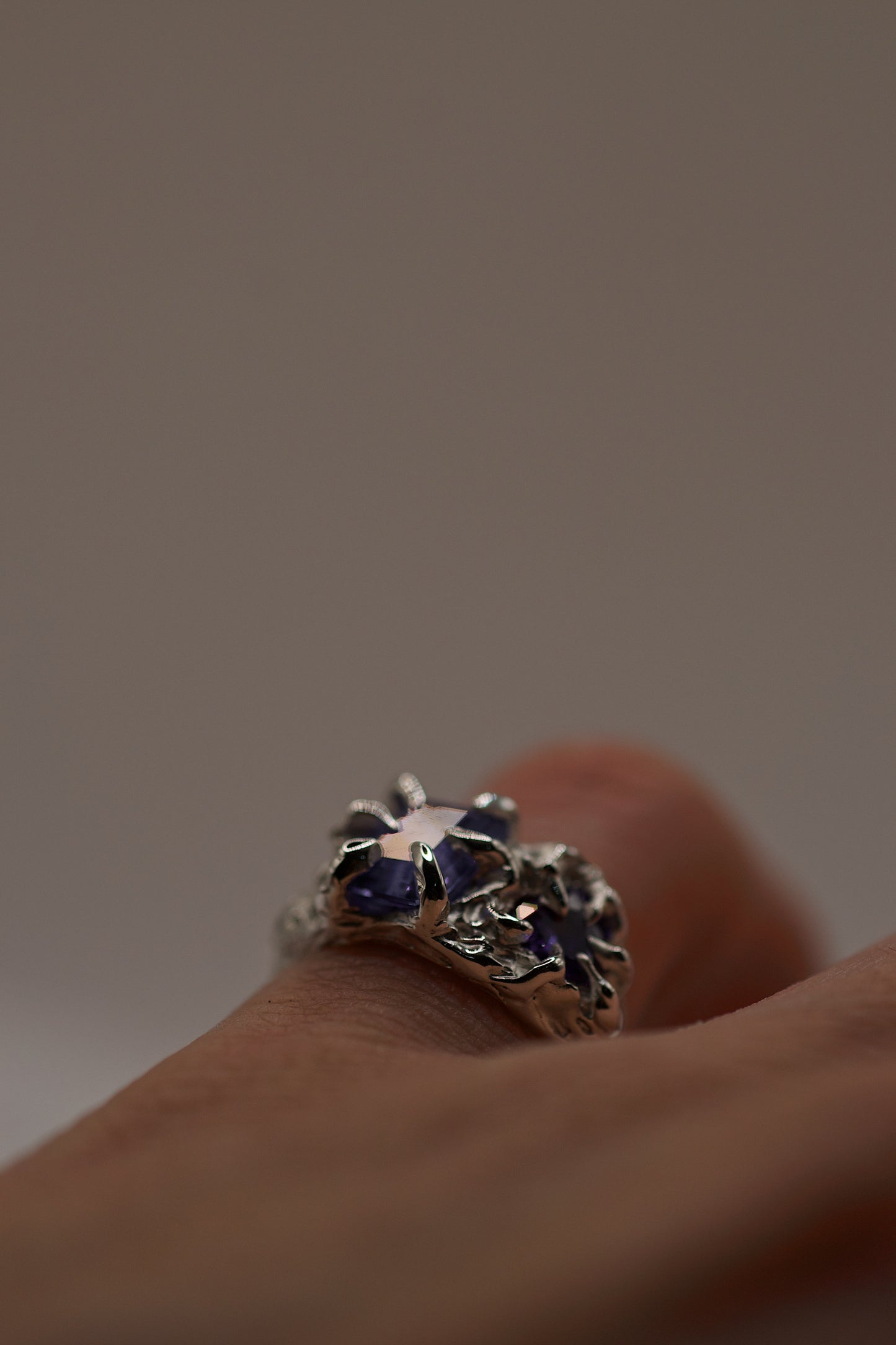 Silver gothic ring worn on a finger, showing how the handmade gothic-style claws hold multiple purple gemstones. The texture and asymmetry emphasize its organic nature, crafted using the lost wax casting technique.