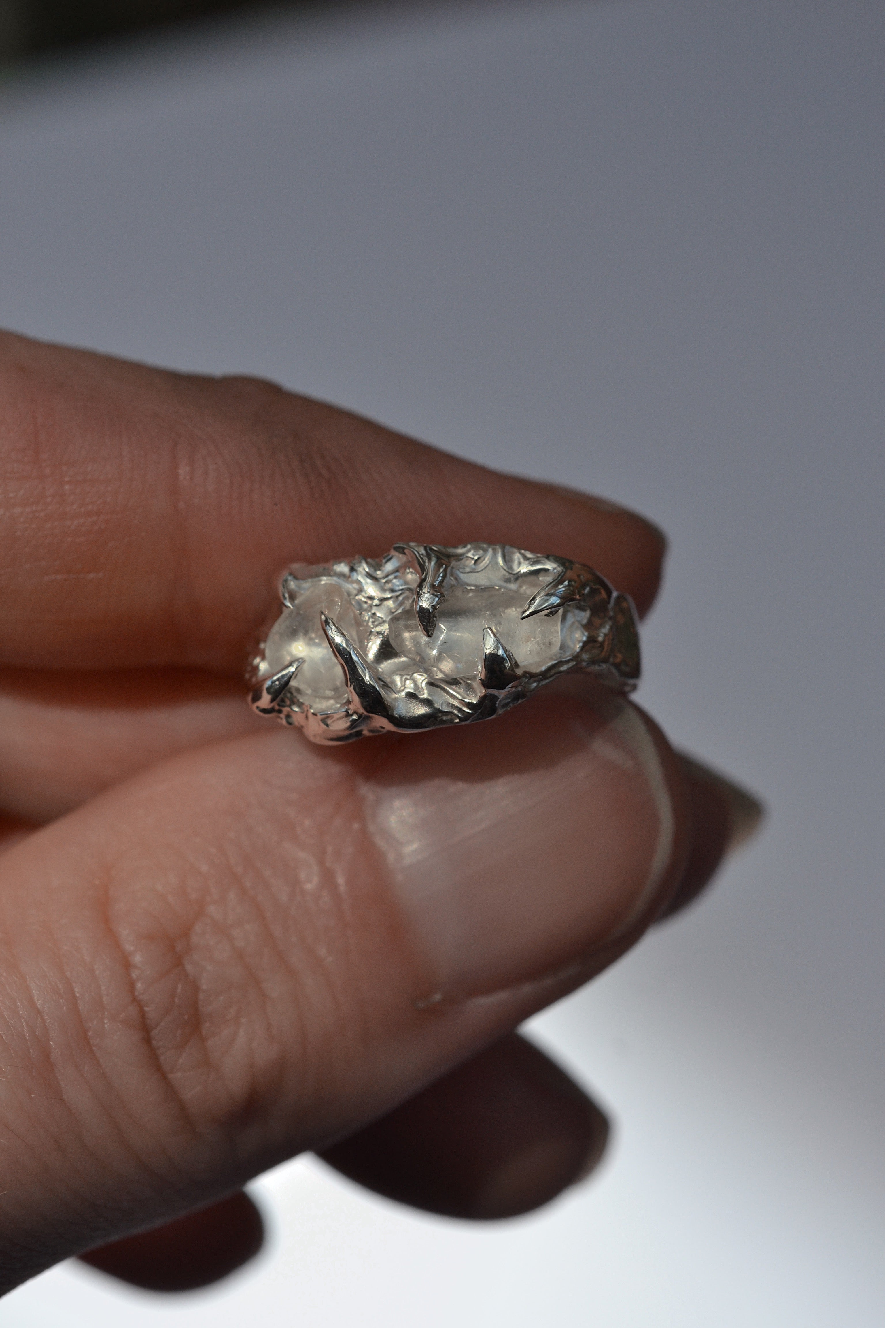 Lost wax cast silver Remnants Ring held in hand with raw quartz crystals and organic molten silver claw setting