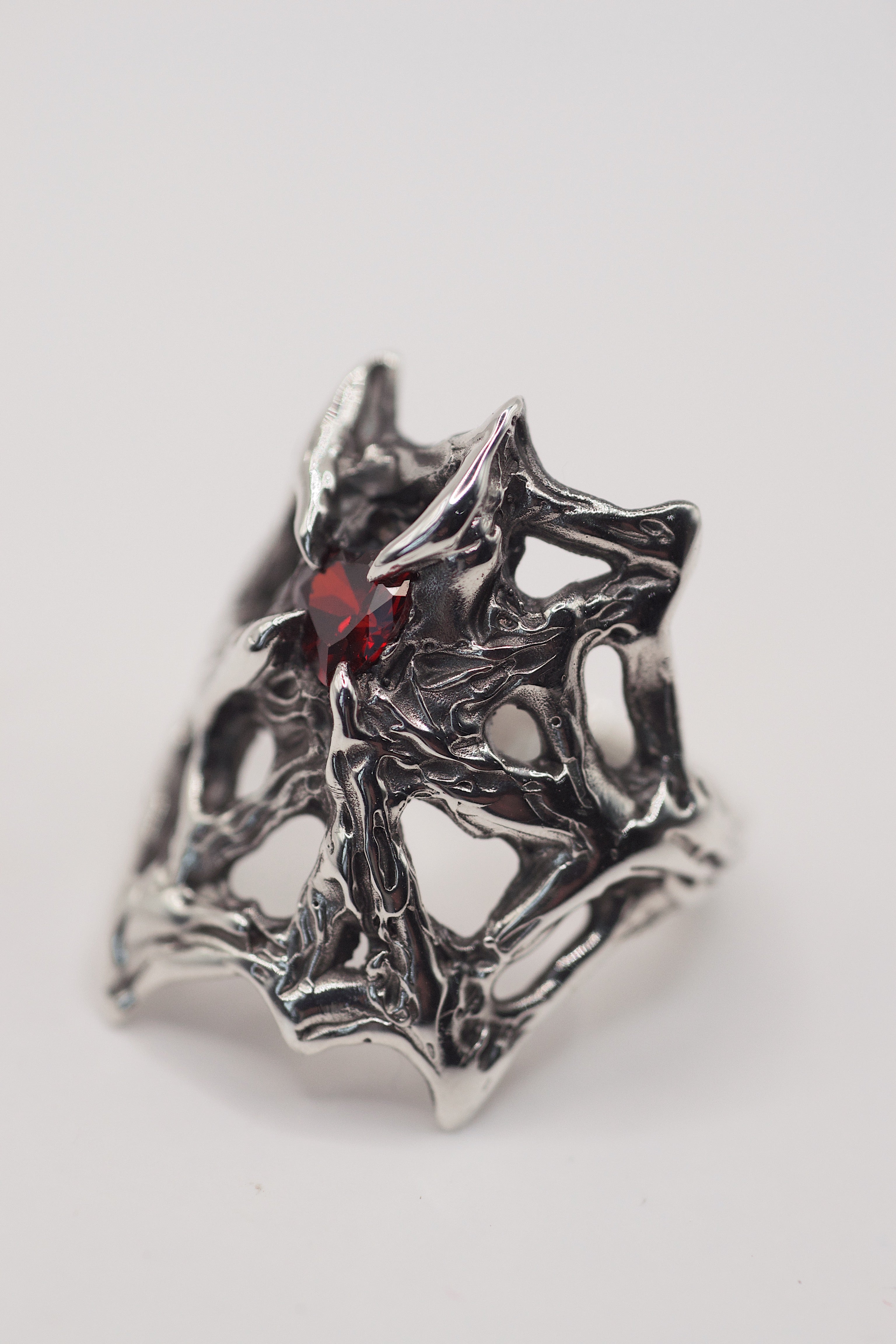 Handmade lost wax cast sterling silver ring with intricate darkened molten web structure gripping a lab-grown red garnet heart, dramatic gothic alternative ring made using the wax carving technique
