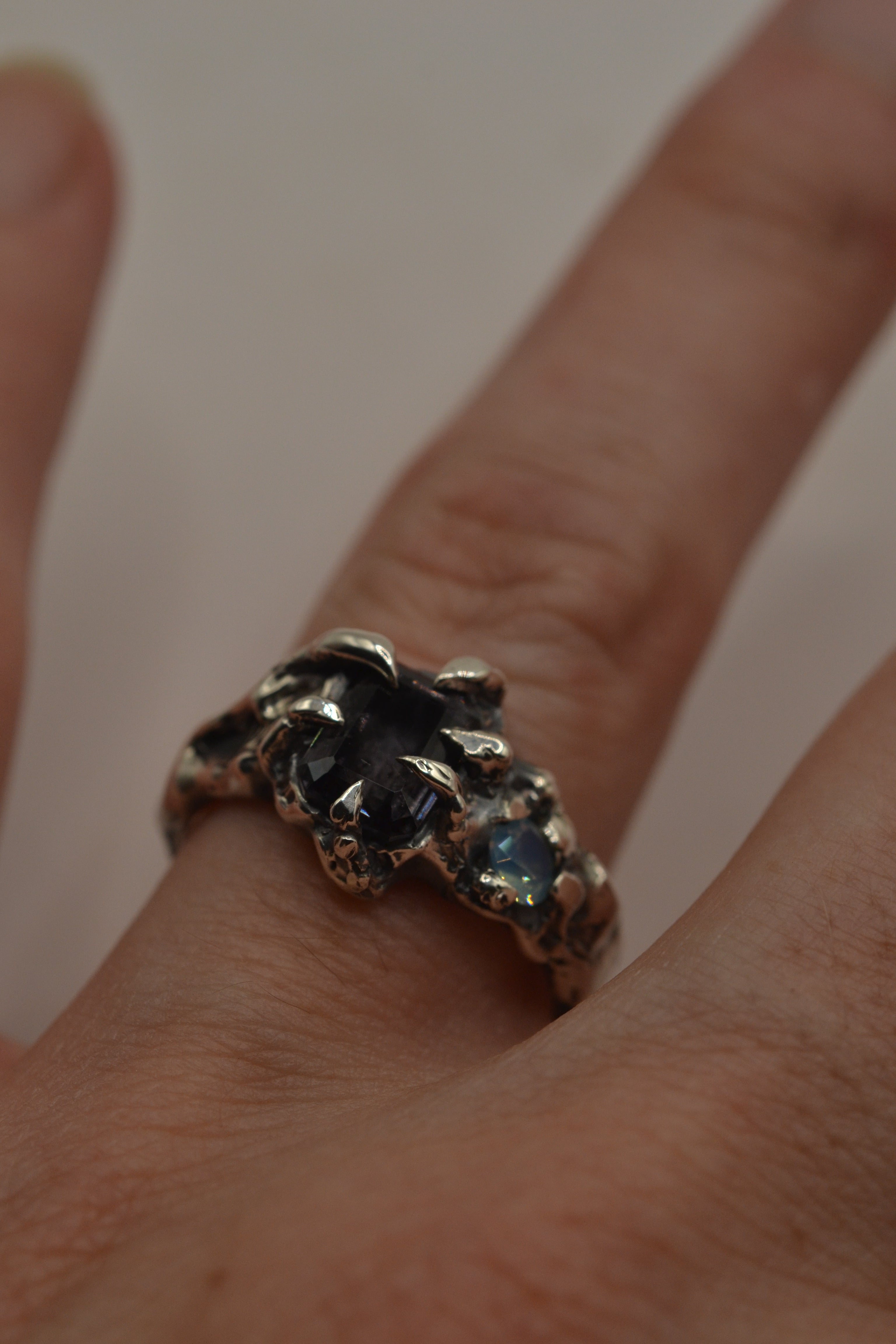 Lost wax cast darkened silver Silhouette Ring worn on hand with milky opal and grey spinel in sculptural darkened claw setting