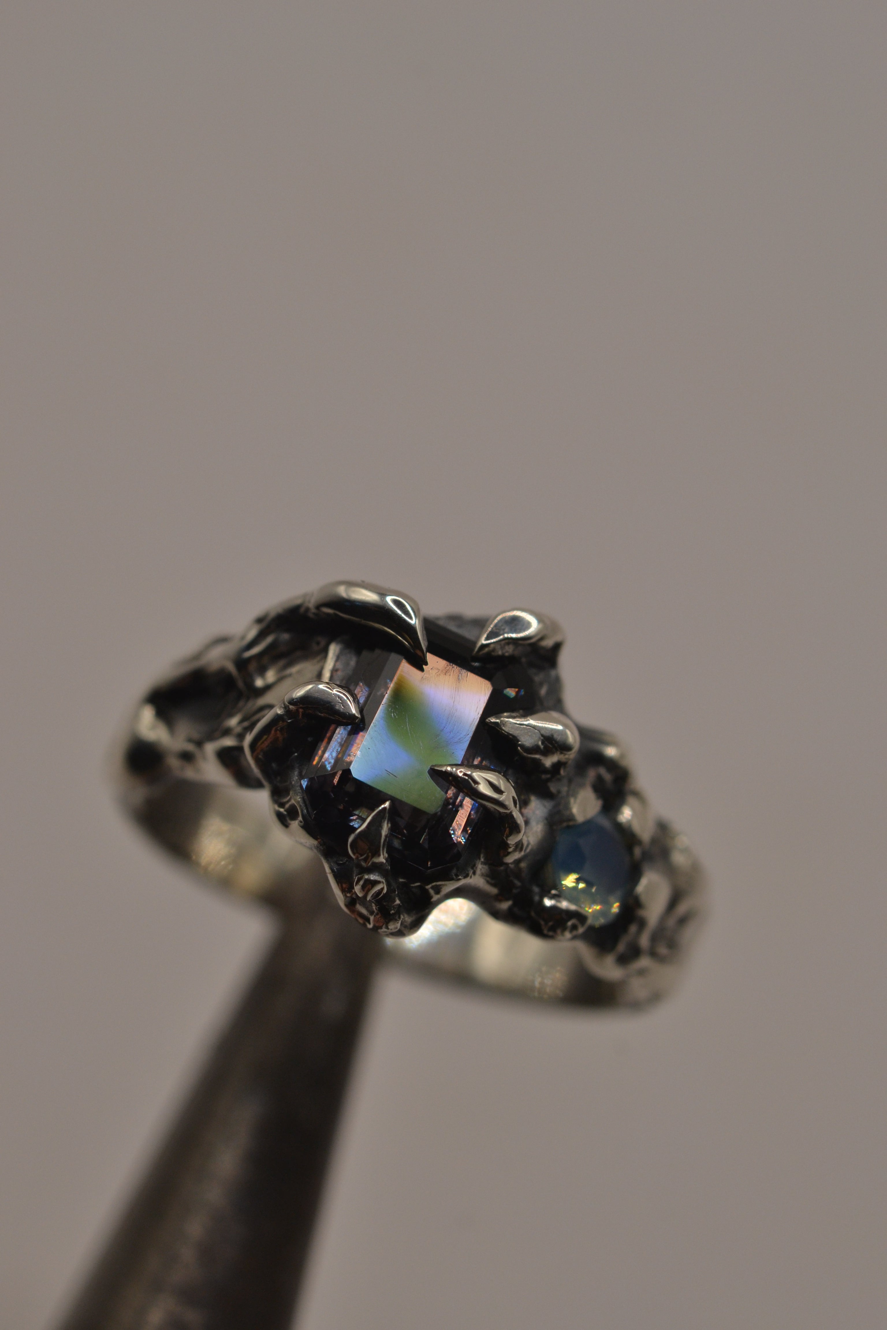 Handmade lost wax cast sterling silver ring with six sculptural darkened claws grasping a milky aqua opal and grey lab-grown spinel, dark alternative ring made using the wax carving technique