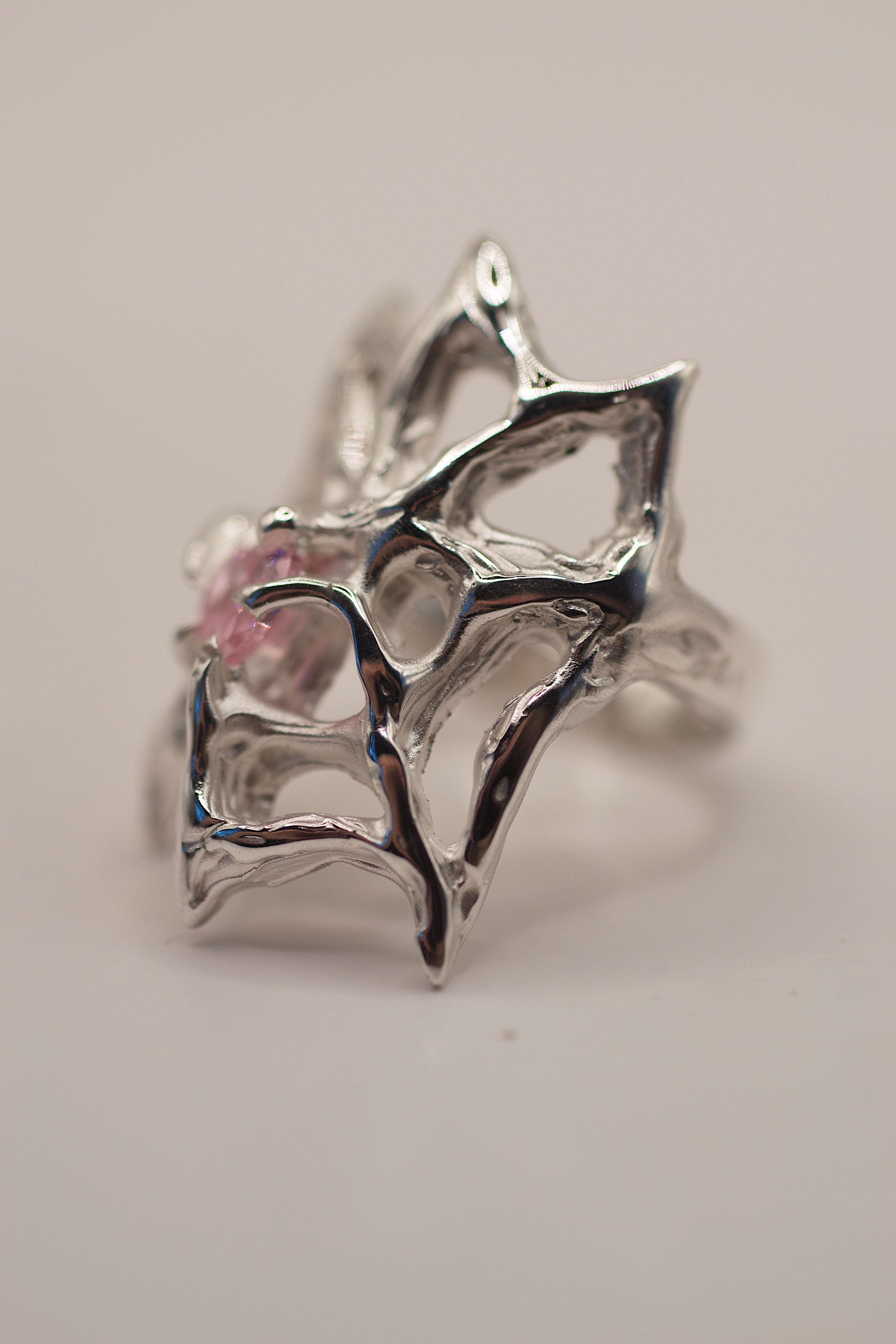 Side angle of the Silk Ring worn on hand showing flowing sterling silver web structure and pink heart cubic zirconia handmade using lost wax casting
