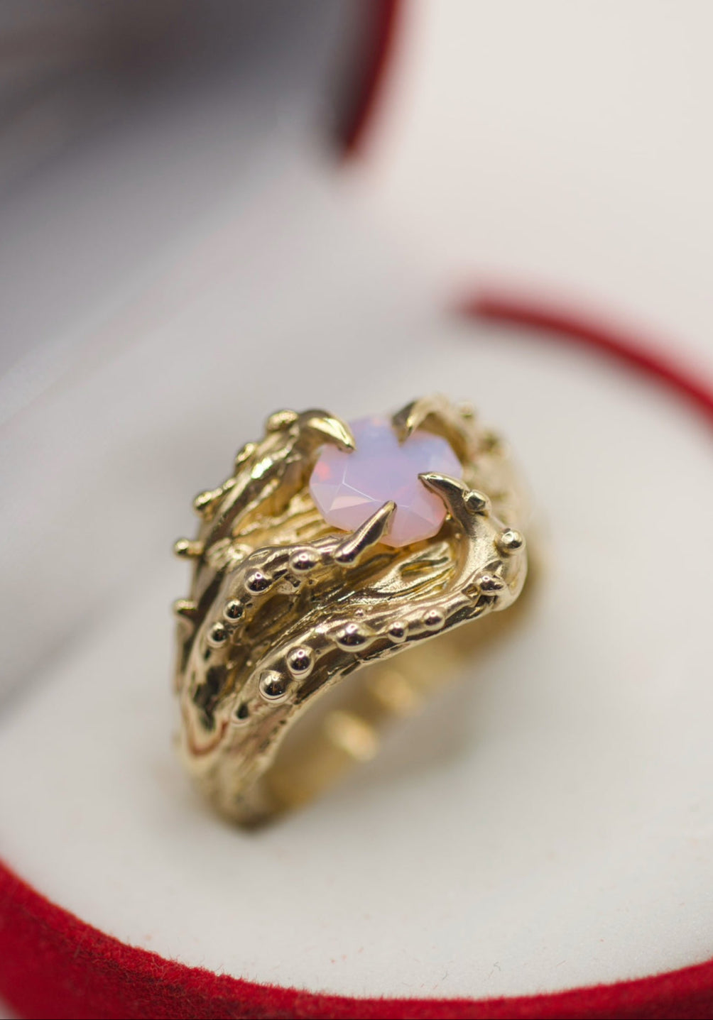 Handmade lost wax cast gold ring with sculptural textured shoulders and four molten claws holding a lab-grown milky pink opal, bold alternative statement ring made using the wax carving technique