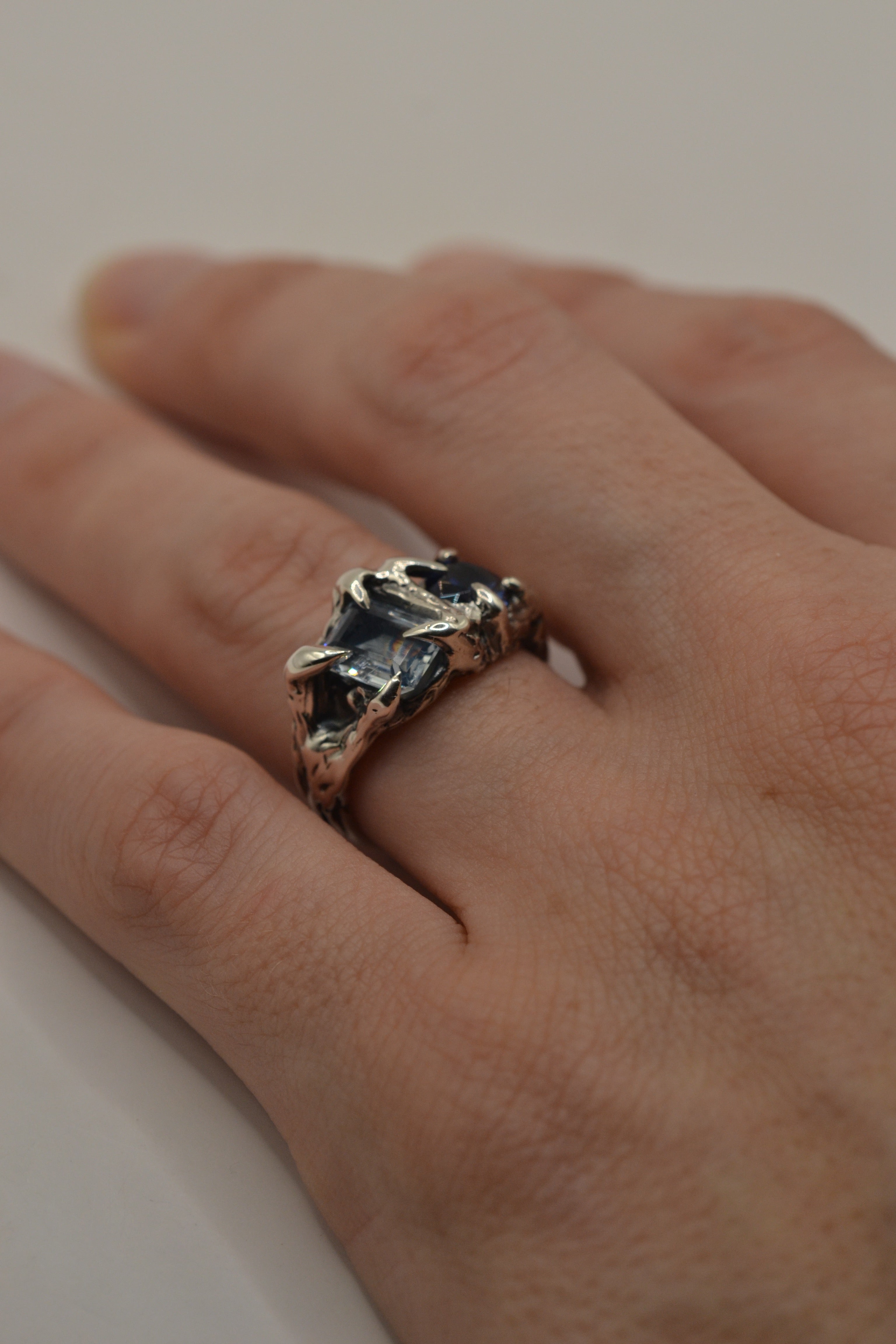 Close up of the Something Blue Ring worn on hand showing natural blue sapphire and topaz set within dimensional darkened sterling silver